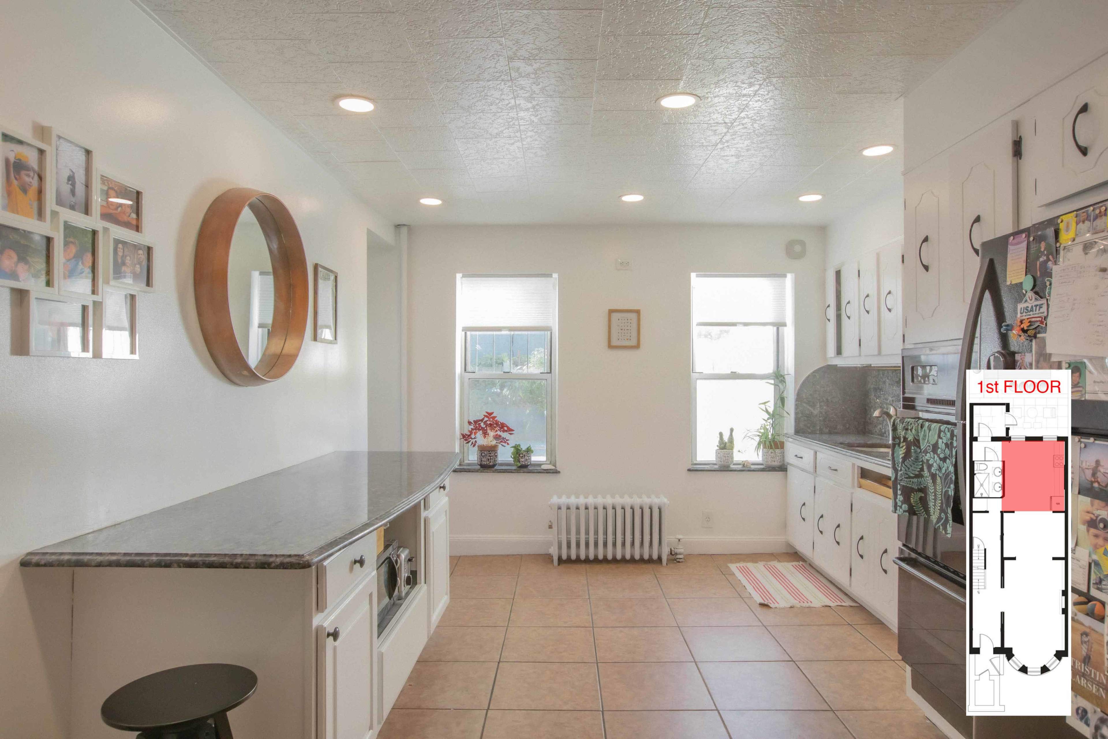 A bright kitchen with white walls, multiple windows, a granite countertop, and a layout plan on the right side.