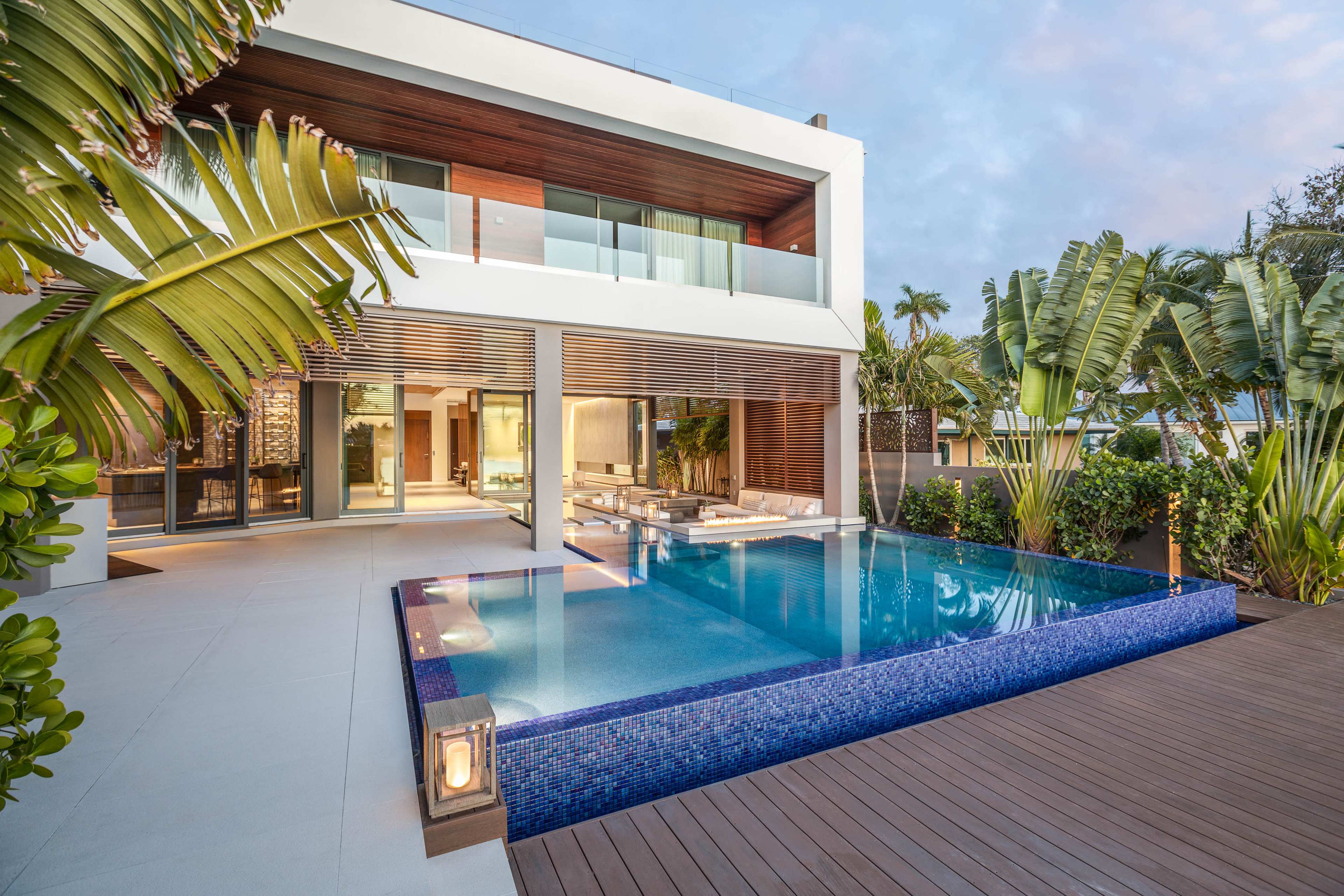A modern villa with a swimming pool surrounded by tropical plants and palm trees.