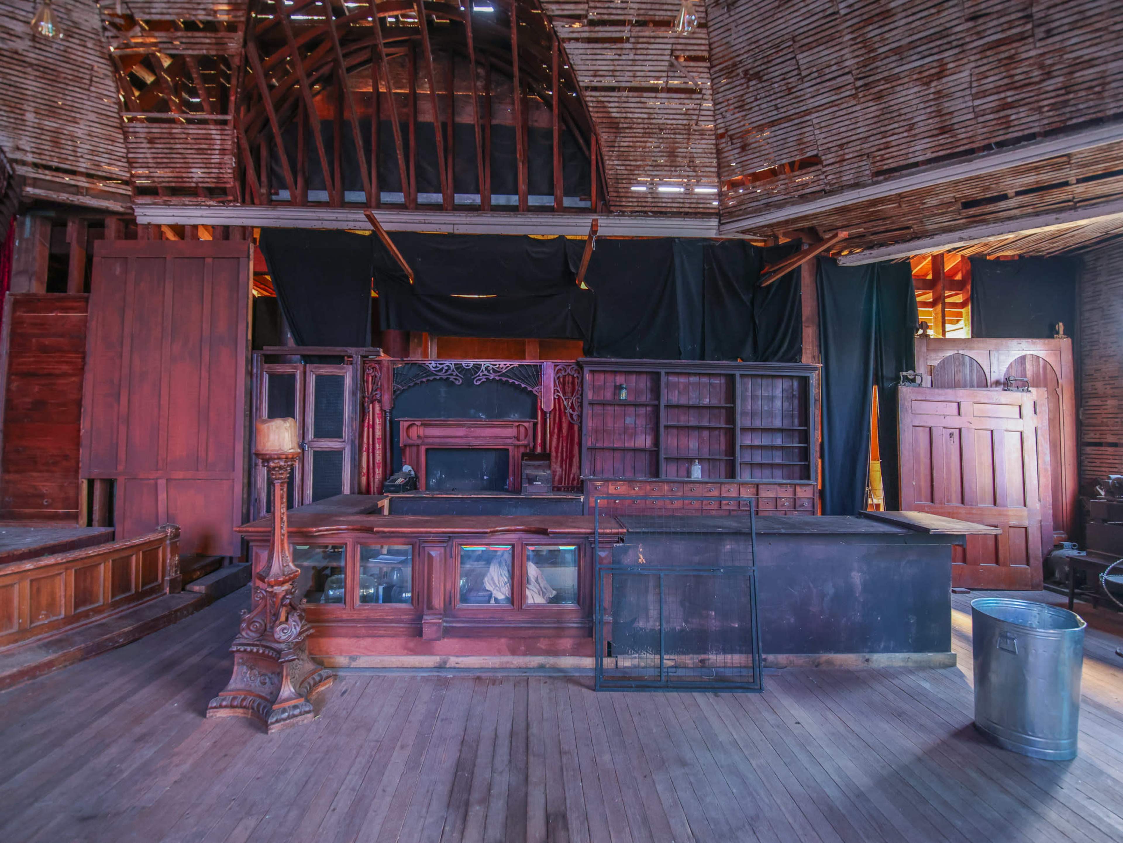 An interior of an abandoned building featuring wooden furniture, empty shelves, and various doors arranged against the walls.