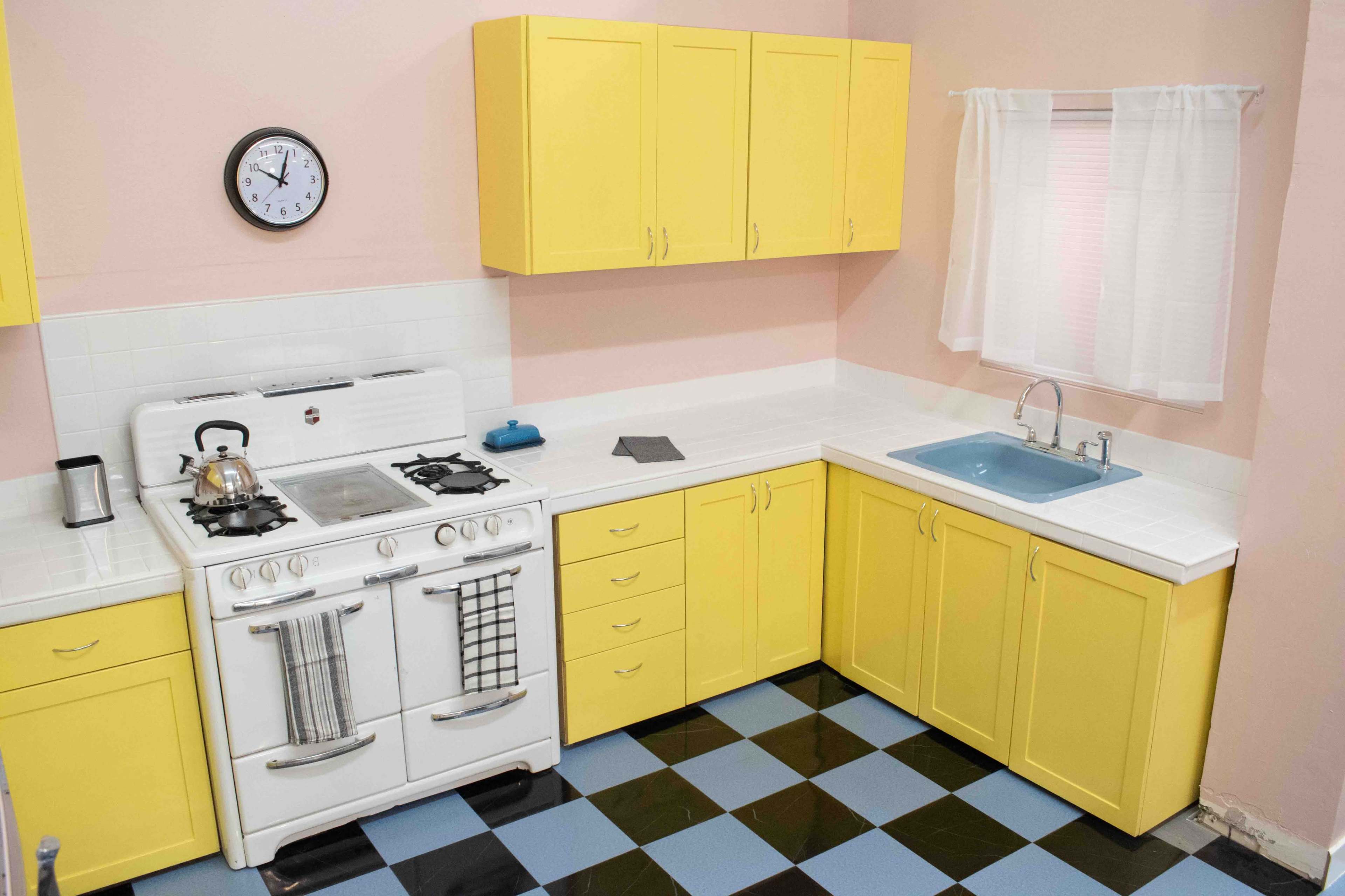 A kitchen with yellow cabinets, a white stove, a sink with a blue basin, and a checkered blue and black floor.