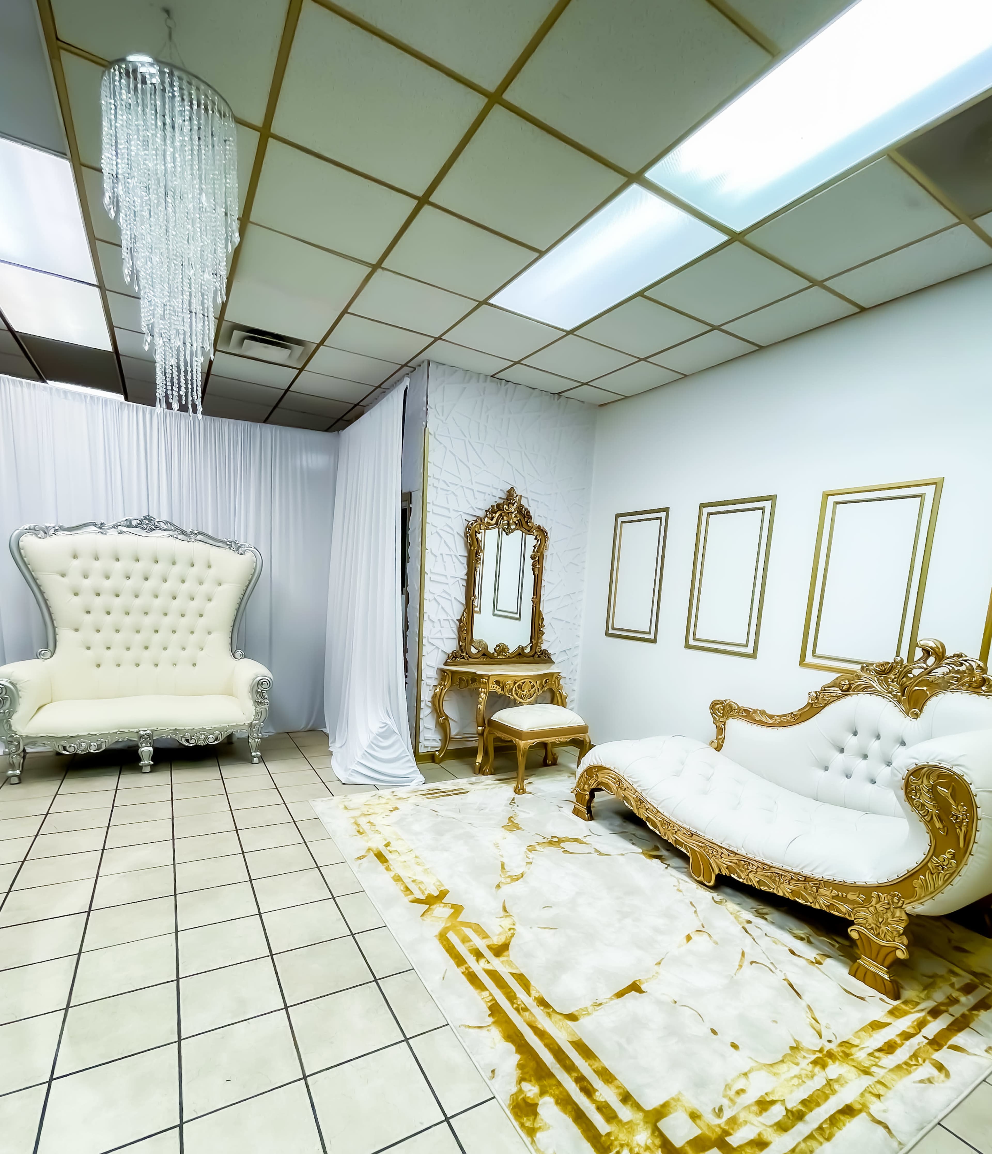 An elegantly furnished room with a white and gold color scheme, featuring ornate furniture, a large chandelier, and empty picture frames on the walls.