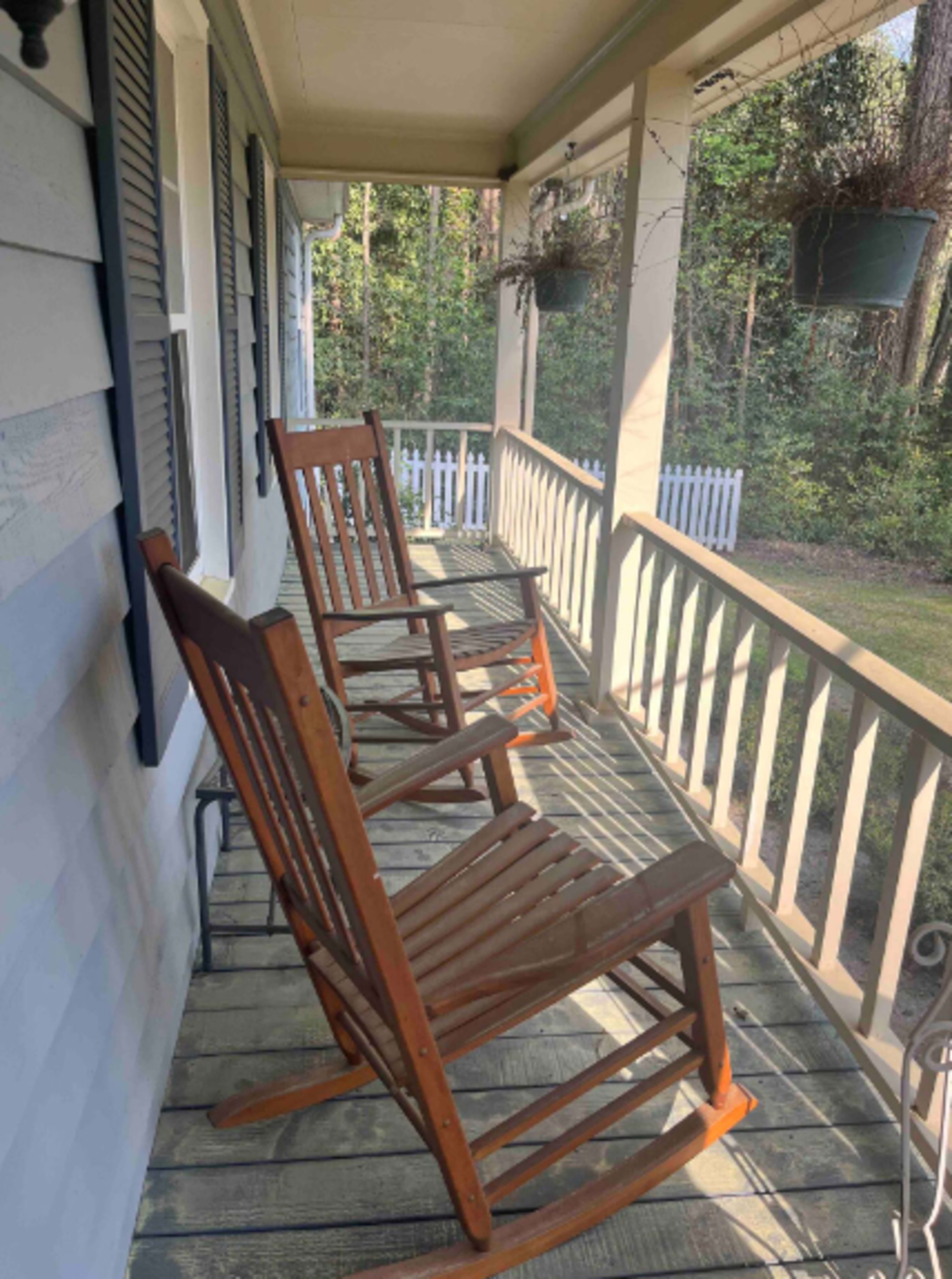 The image shows two wooden rocking chairs on a porch, surrounded by trees and greenery.