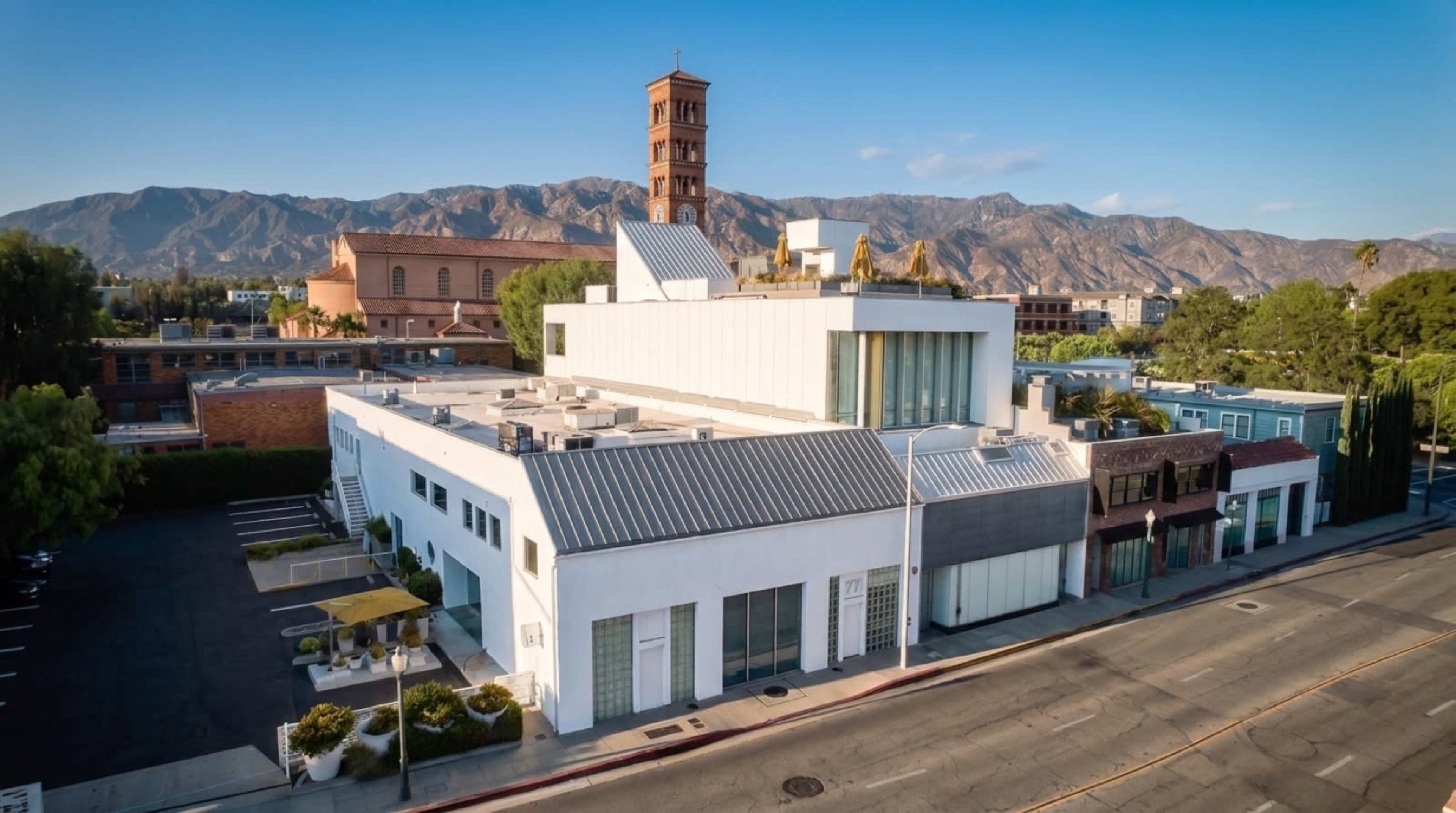 The image shows a modern building with a sleek design in the foreground, set against a backdrop of mountains and a historical church tower in the background.