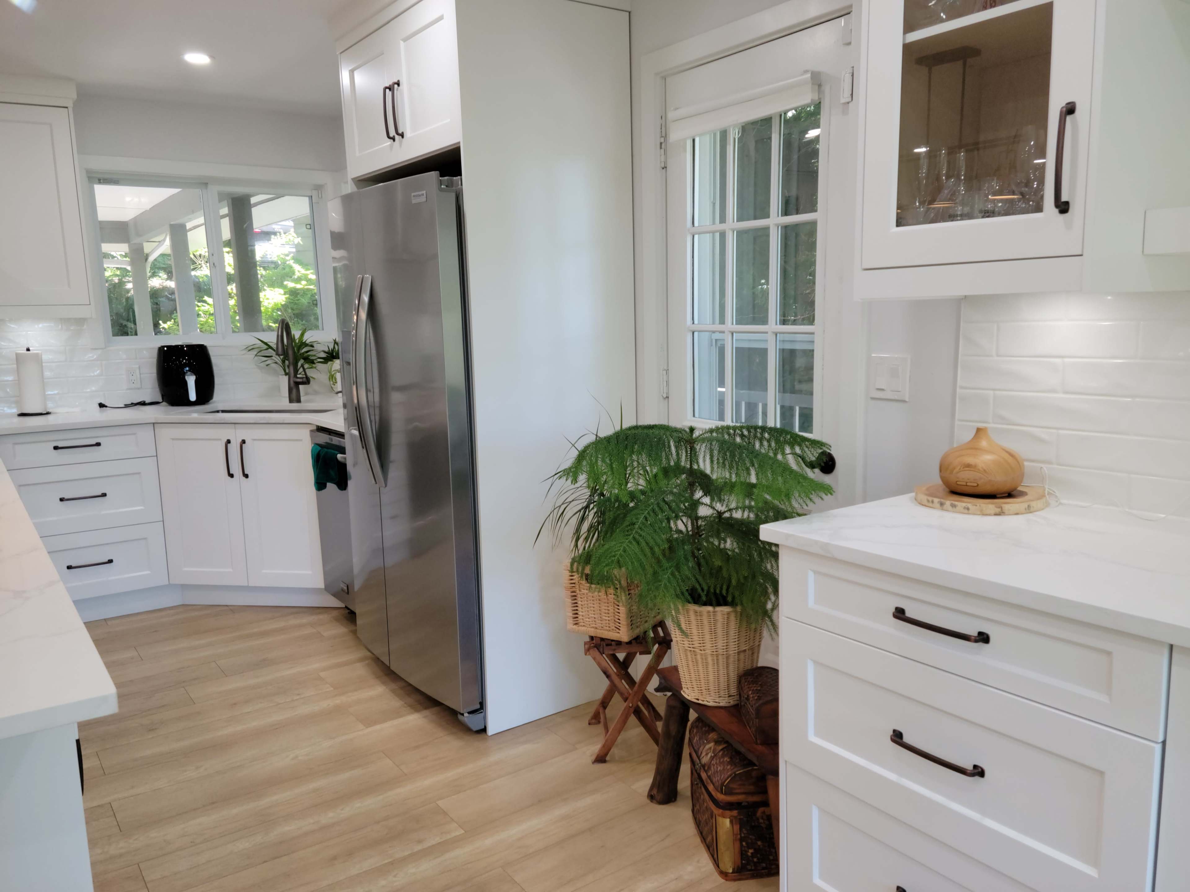 A modern kitchen with white cabinetry, a stainless steel refrigerator, and a potted plant near a window.