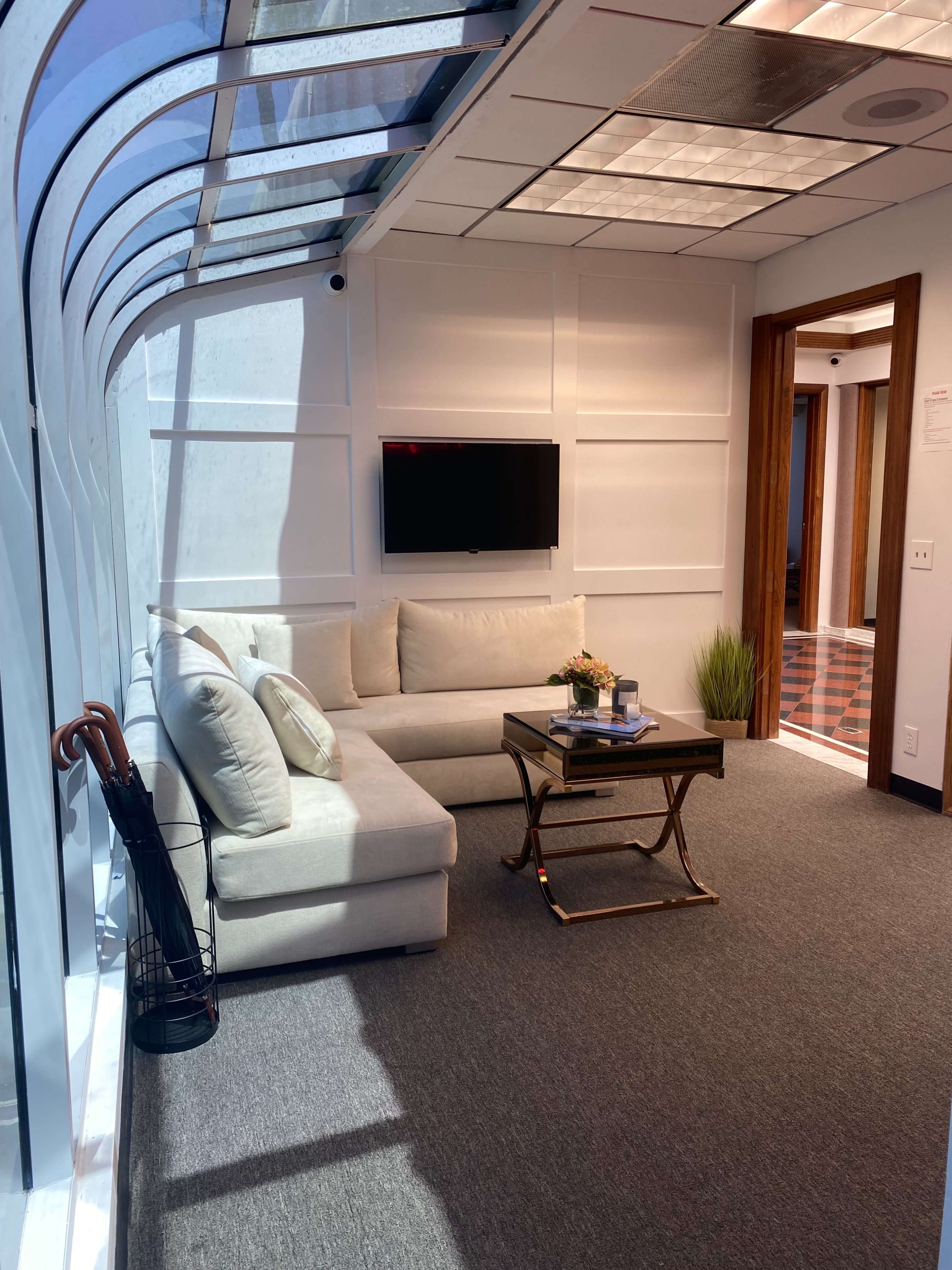 A modern lounge area features a sectional sofa, a coffee table, and a wall-mounted television, with large windows allowing natural light to fill the space.