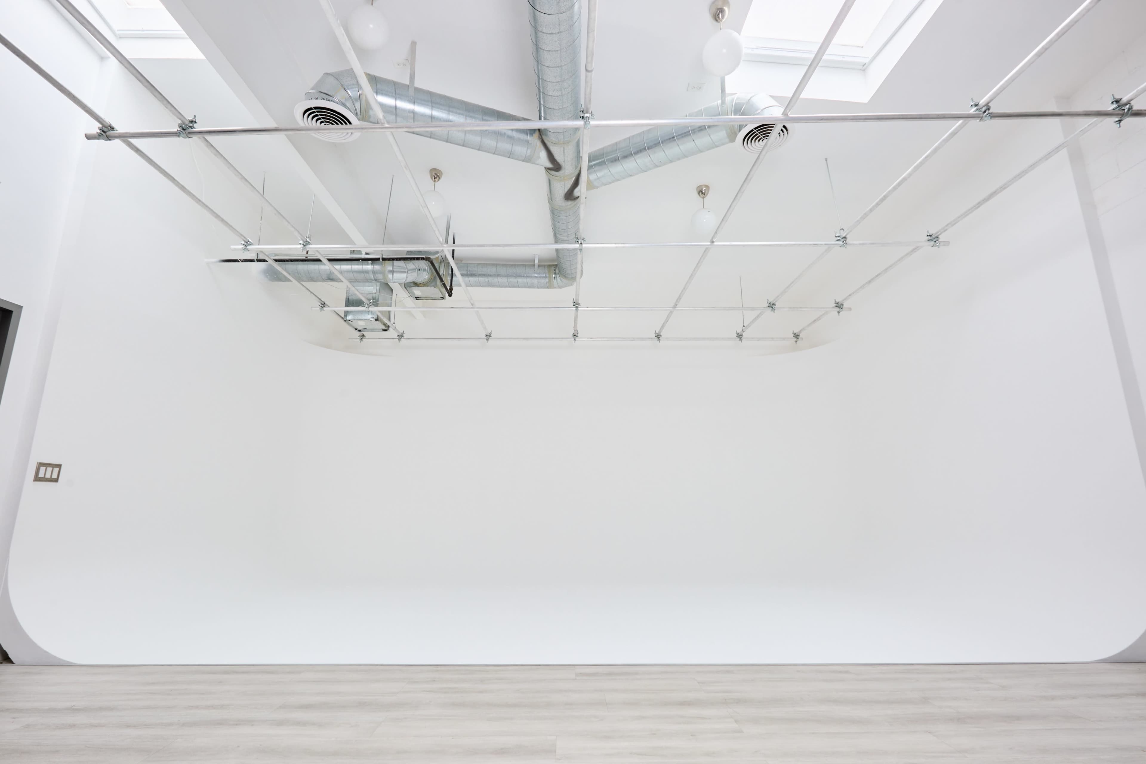 The image shows a spacious, minimalistic studio with a seamless white backdrop and exposed ductwork on the ceiling.