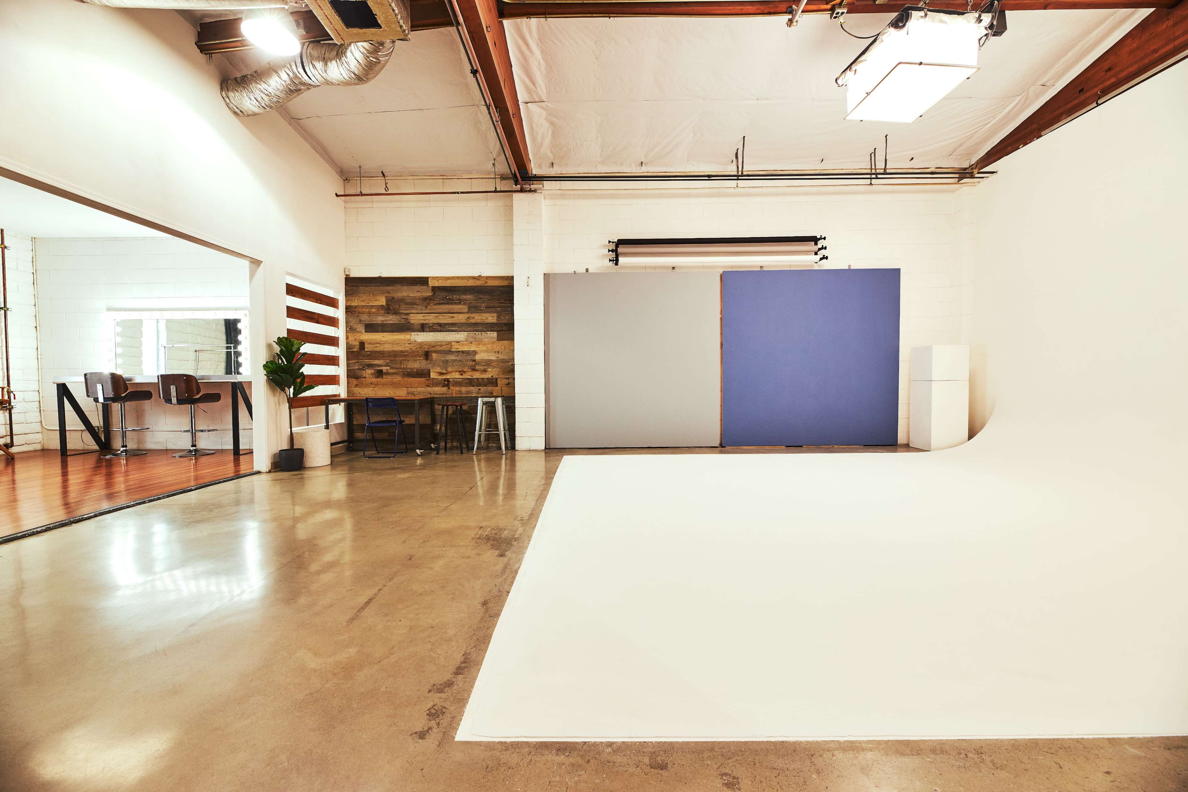 A spacious photo studio with a white backdrop, polished concrete floor, and wooden wall accents.