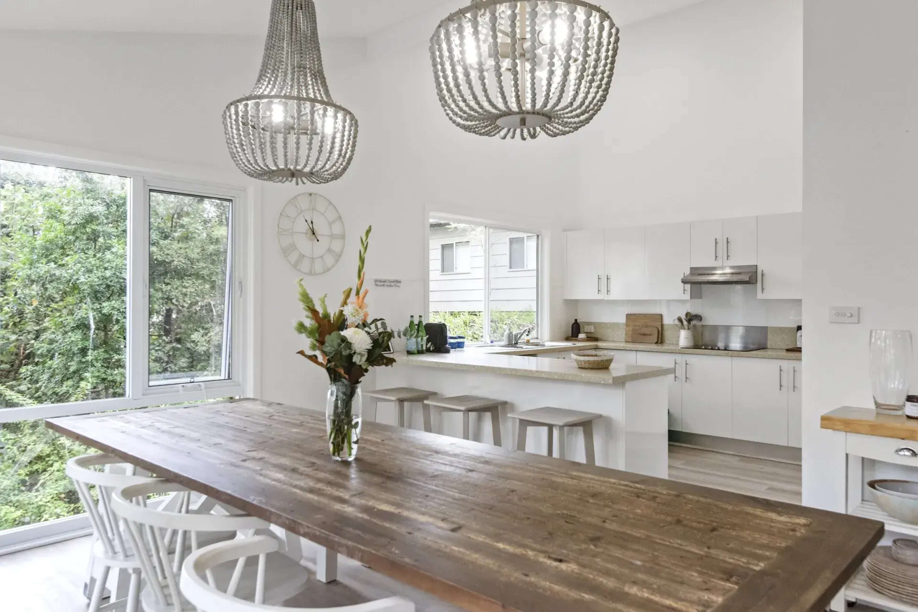 A modern kitchen with a large wooden dining table, white cabinetry, and three pendant lights hanging from the ceiling.