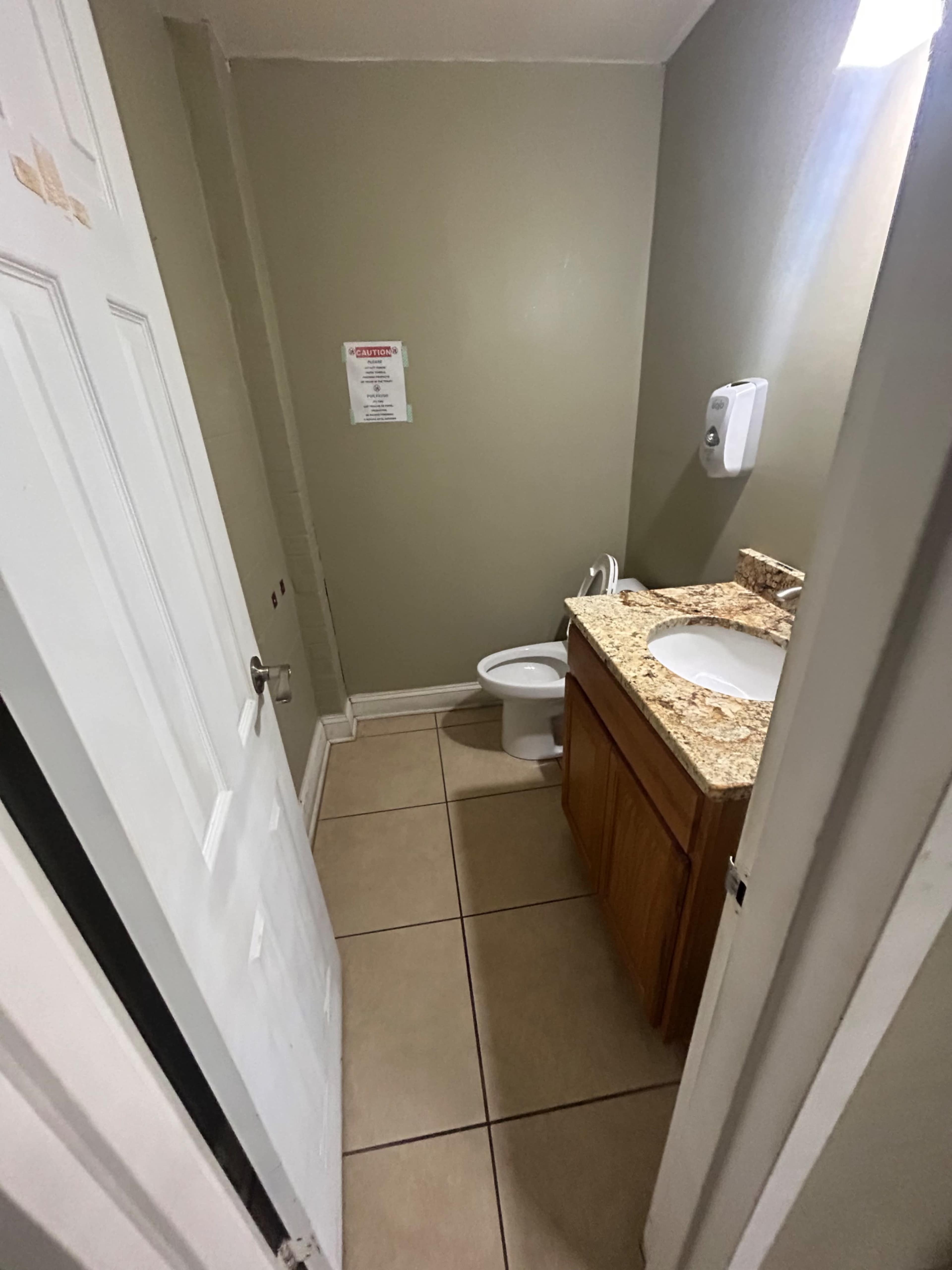 A small bathroom with a toilet, sink, and a door leading to the outside.