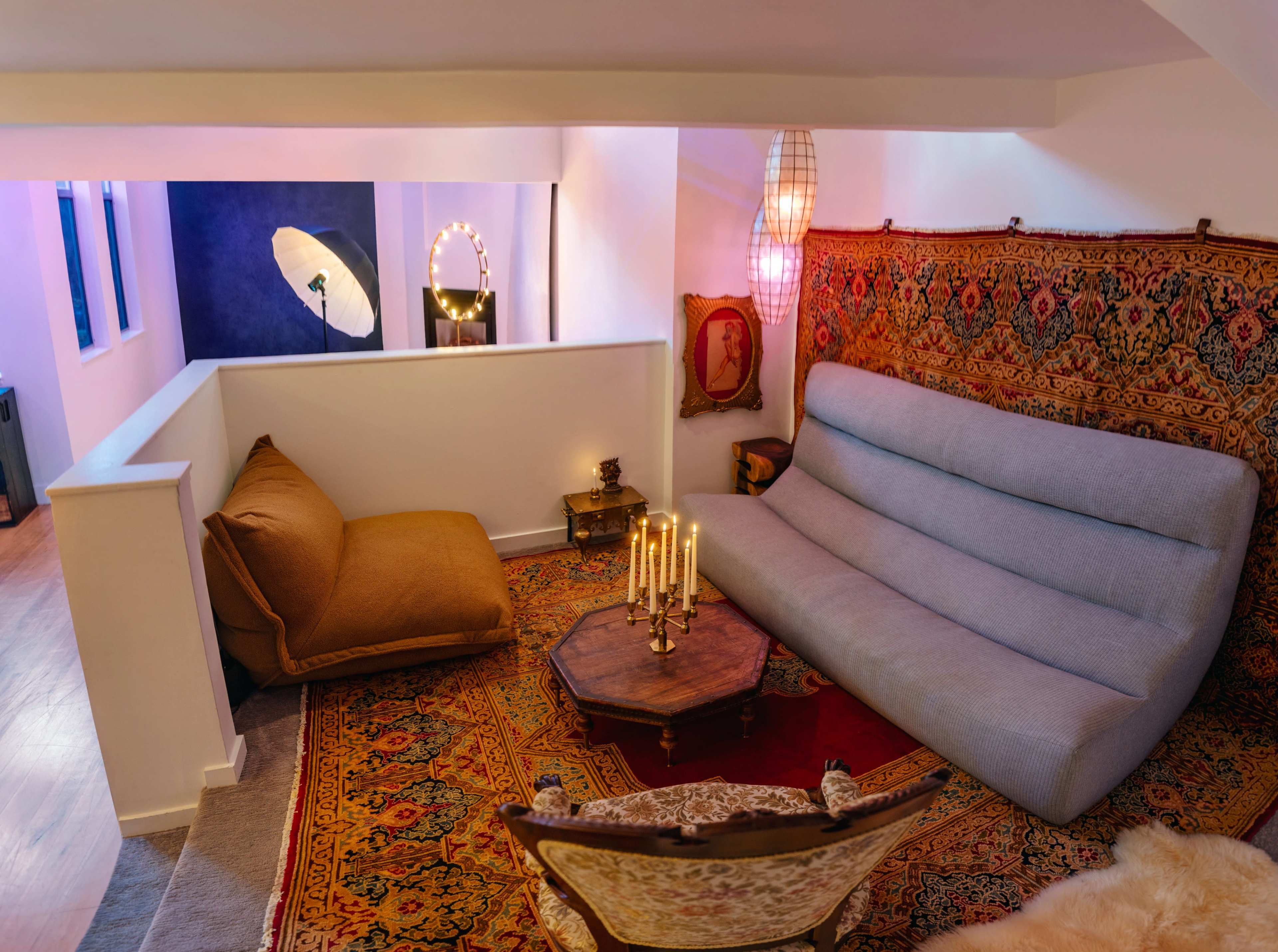 The image shows a cozy living area with modern and vintage furniture, featuring a large sofa, an armchair, a coffee table, and decorative items on a patterned rug.