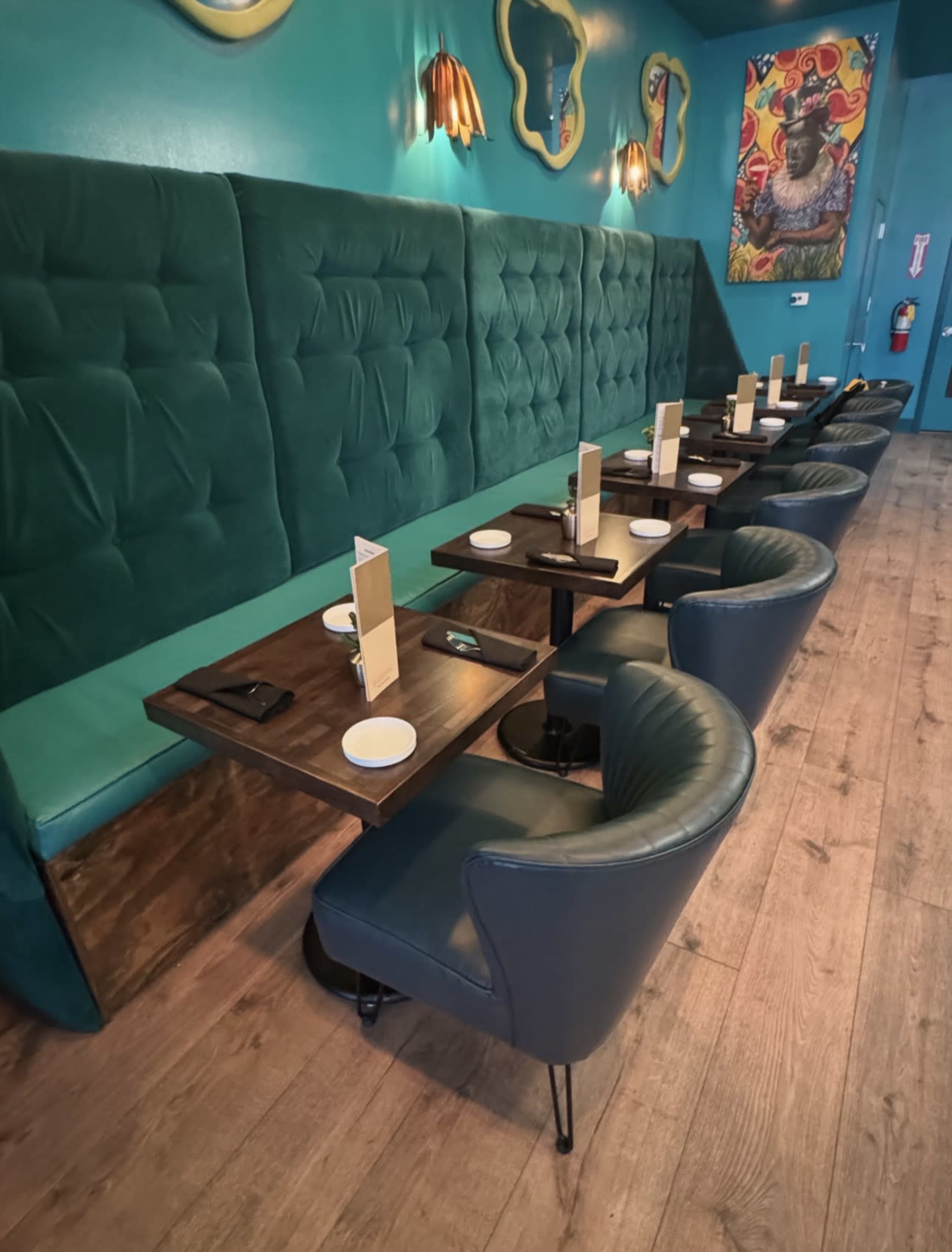 The image shows a restaurant interior with green upholstered walls, blue chairs, and tables neatly set for dining.