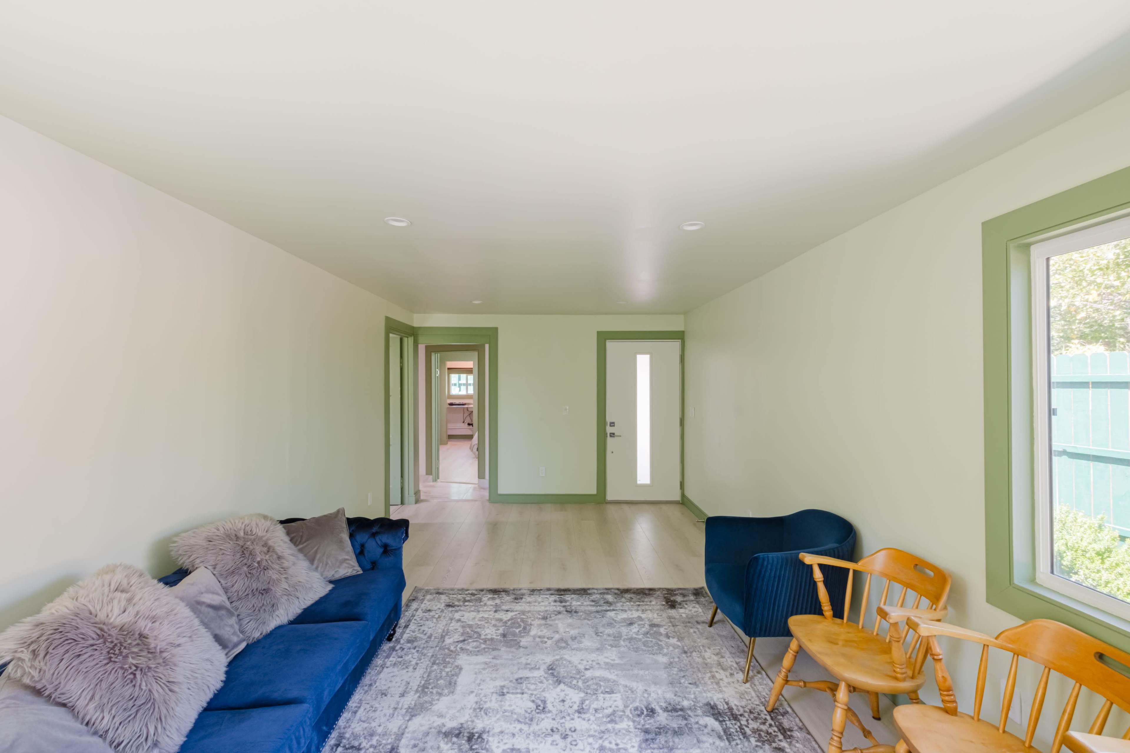 A minimalist living room with a blue sofa, two wooden chairs, and a light-colored rug on a hardwood floor.
