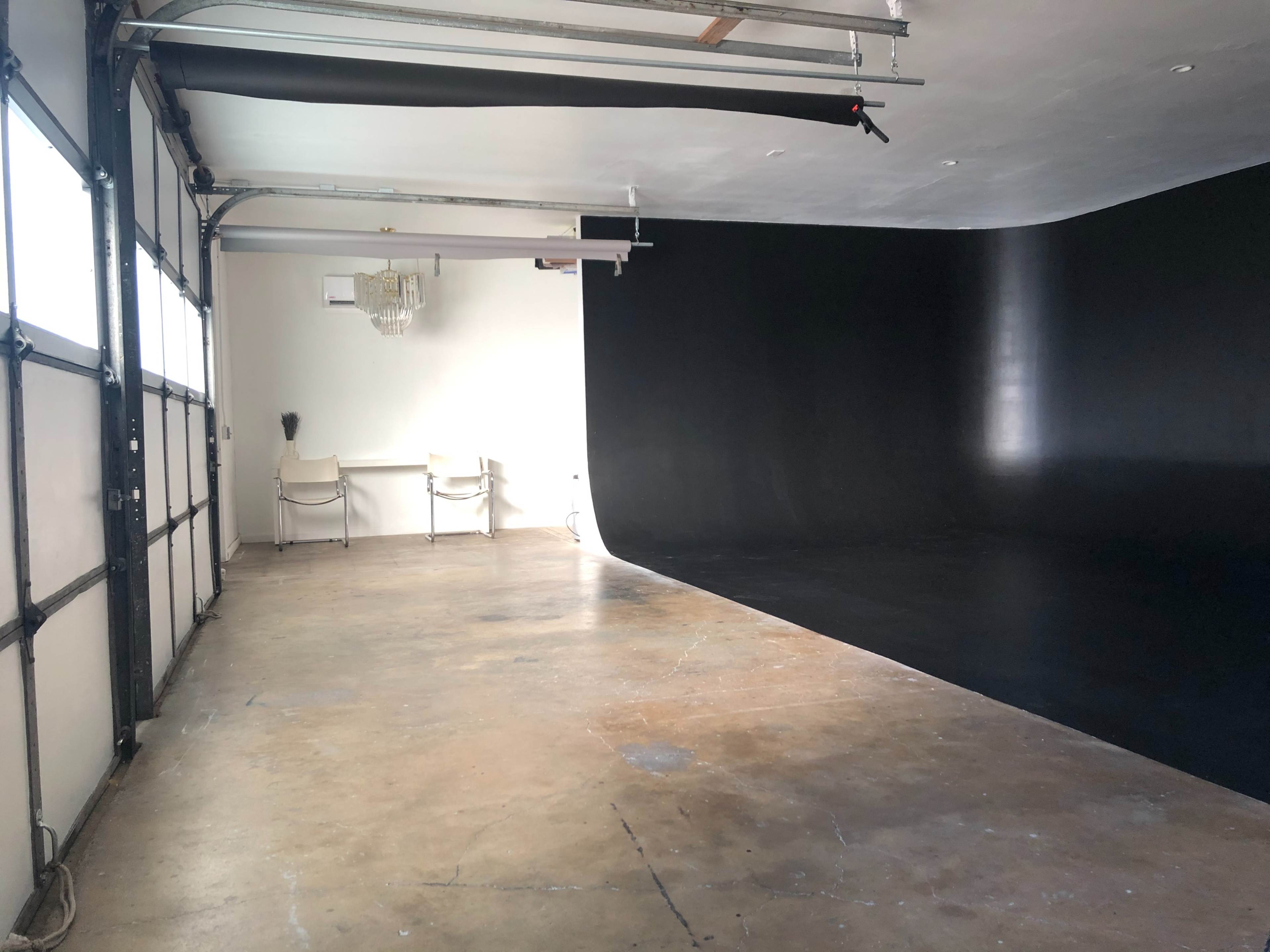 A spacious studio with a black backdrop, polished concrete floor, and a small desk with chairs.