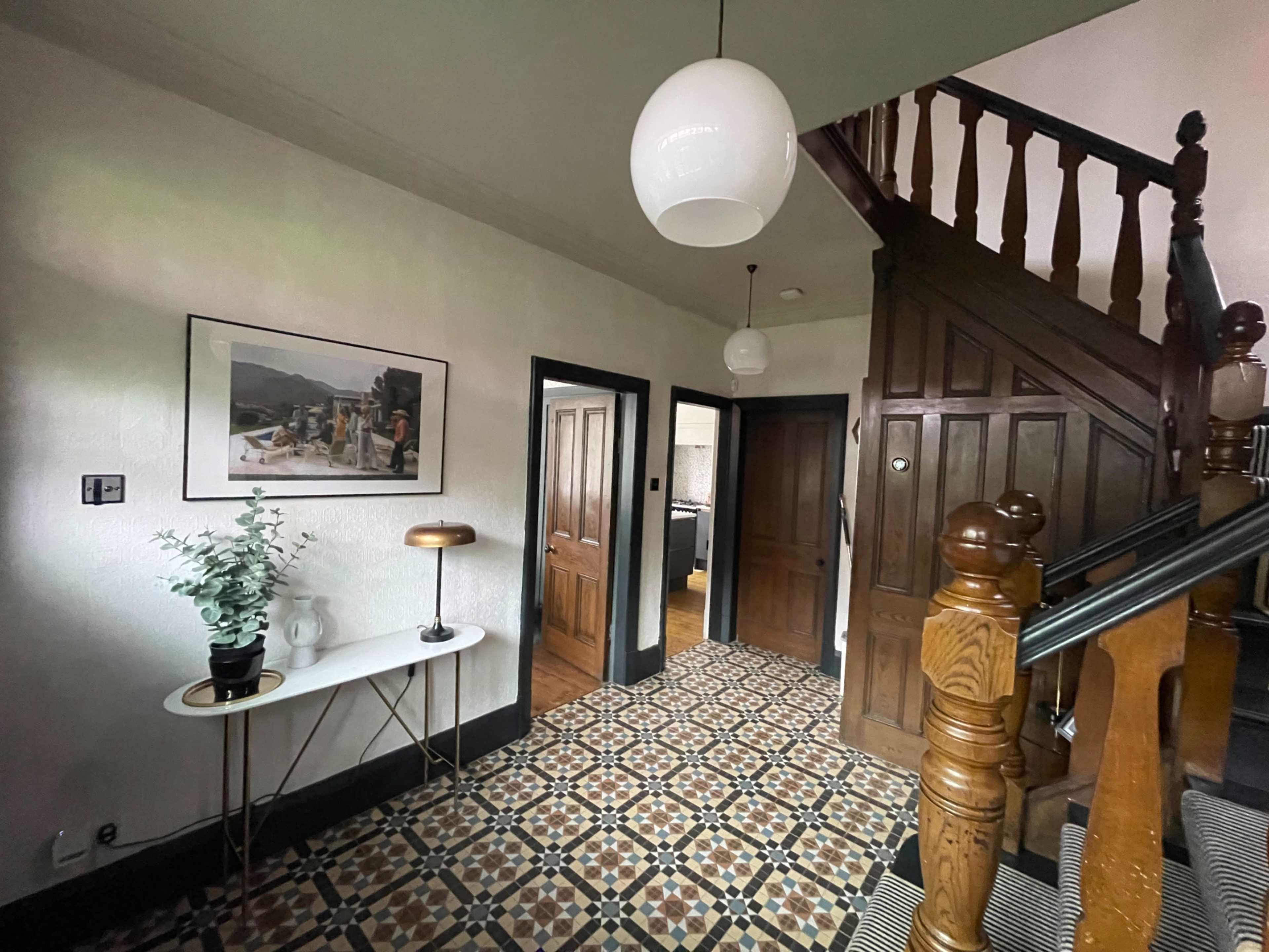The image depicts a hallway with patterned tile flooring, a staircase with wooden railing, and doors leading to different rooms.