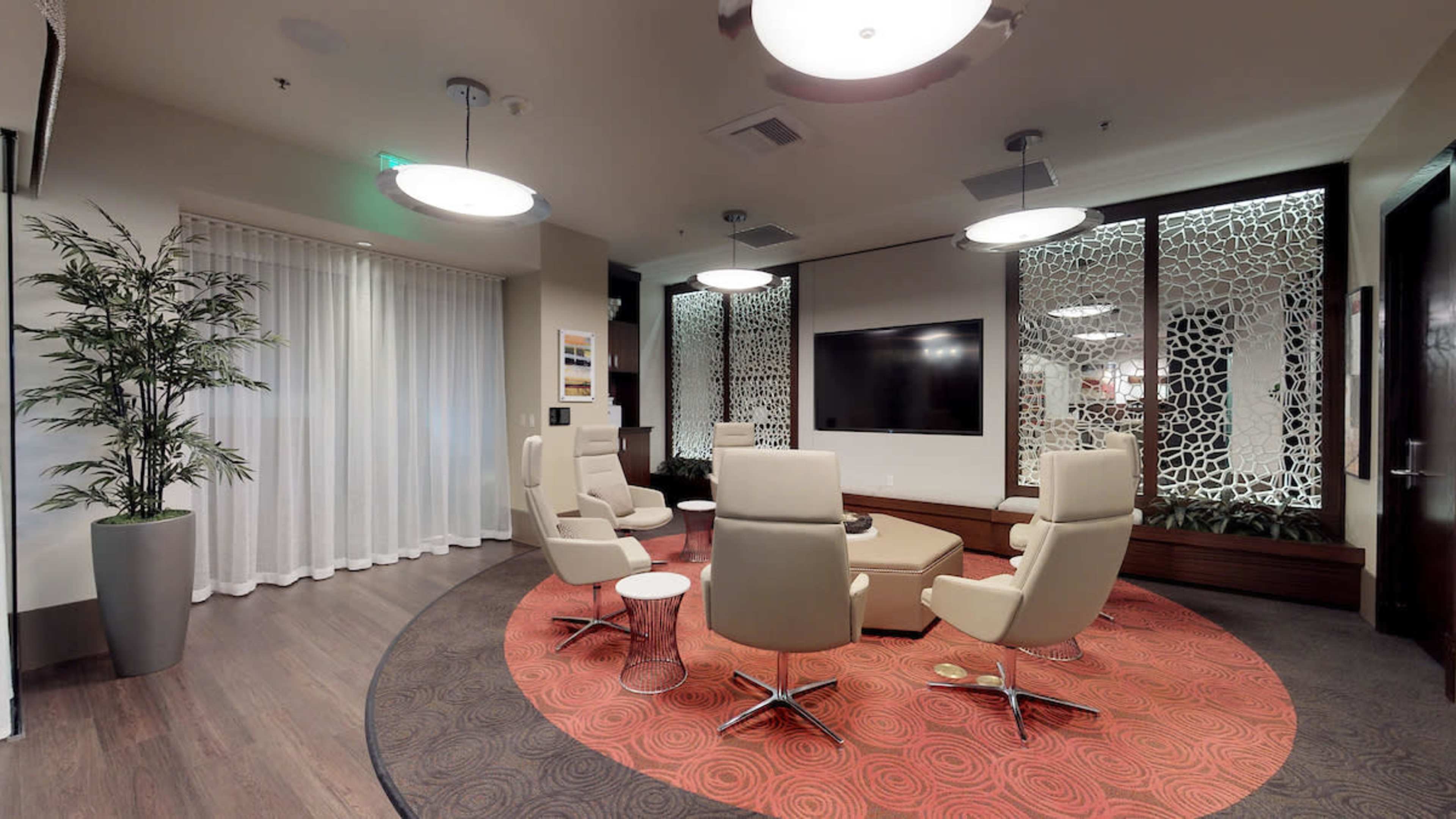 A modern lounge area with circular seating arranged around a coffee table, complemented by decorative screens and large windows.