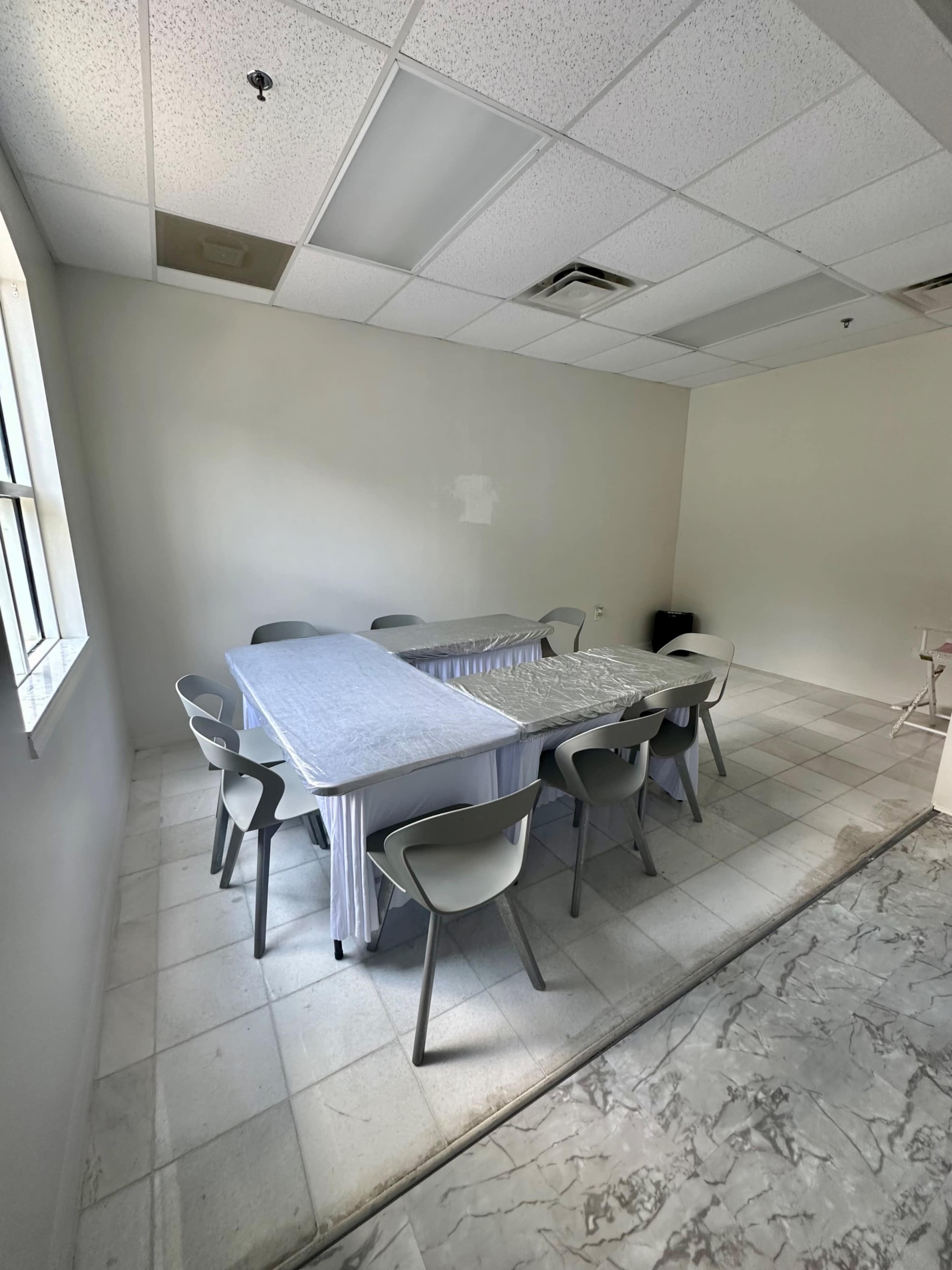 A spacious, empty meeting room features a long table covered with a tablecloth and surrounded by several chairs.