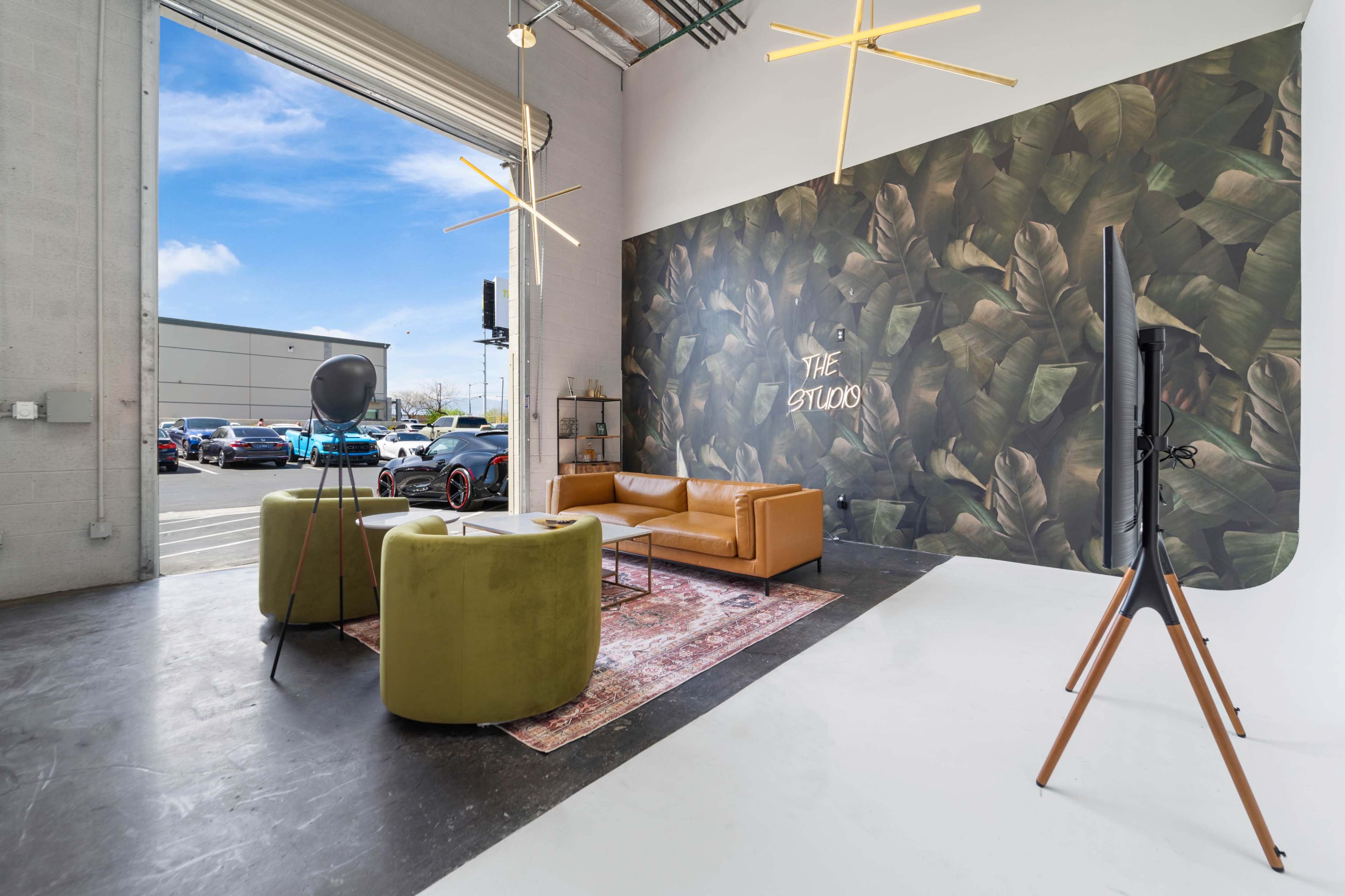 A modern interior space featuring a leather sofa, two green chairs, a large wall with a leafy mural, and a flat-screen television on a wooden stand.
