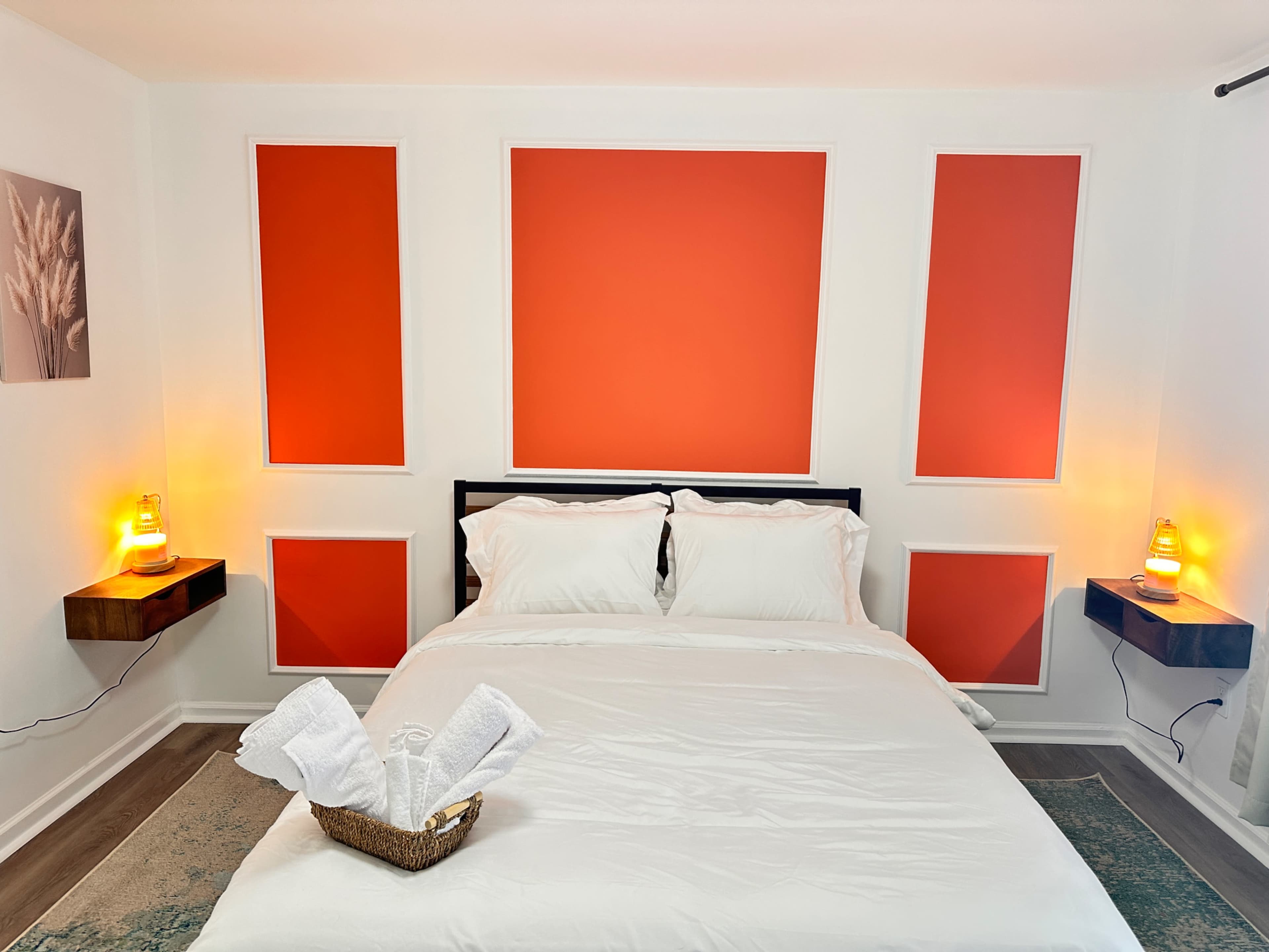 The image depicts a neatly made bed in a room with orange accent walls and two bedside tables, each with a lamp.