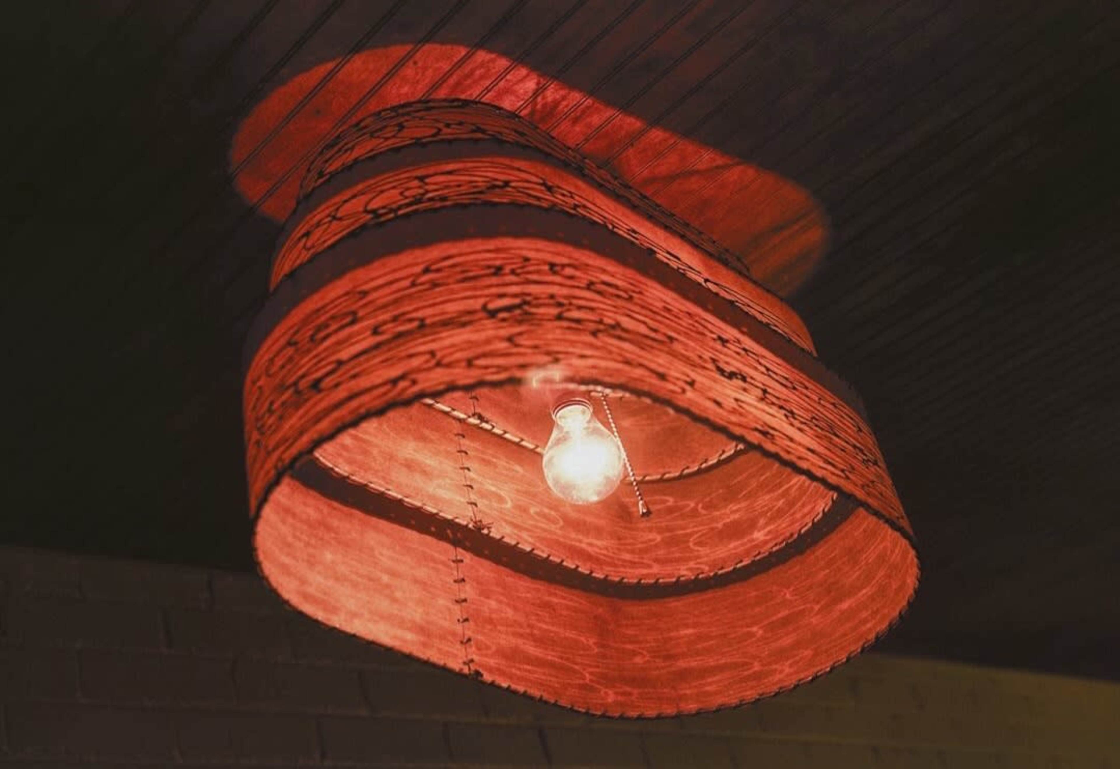 A large red lampshade with a patterned design hangs from the ceiling, enclosing a single light bulb.