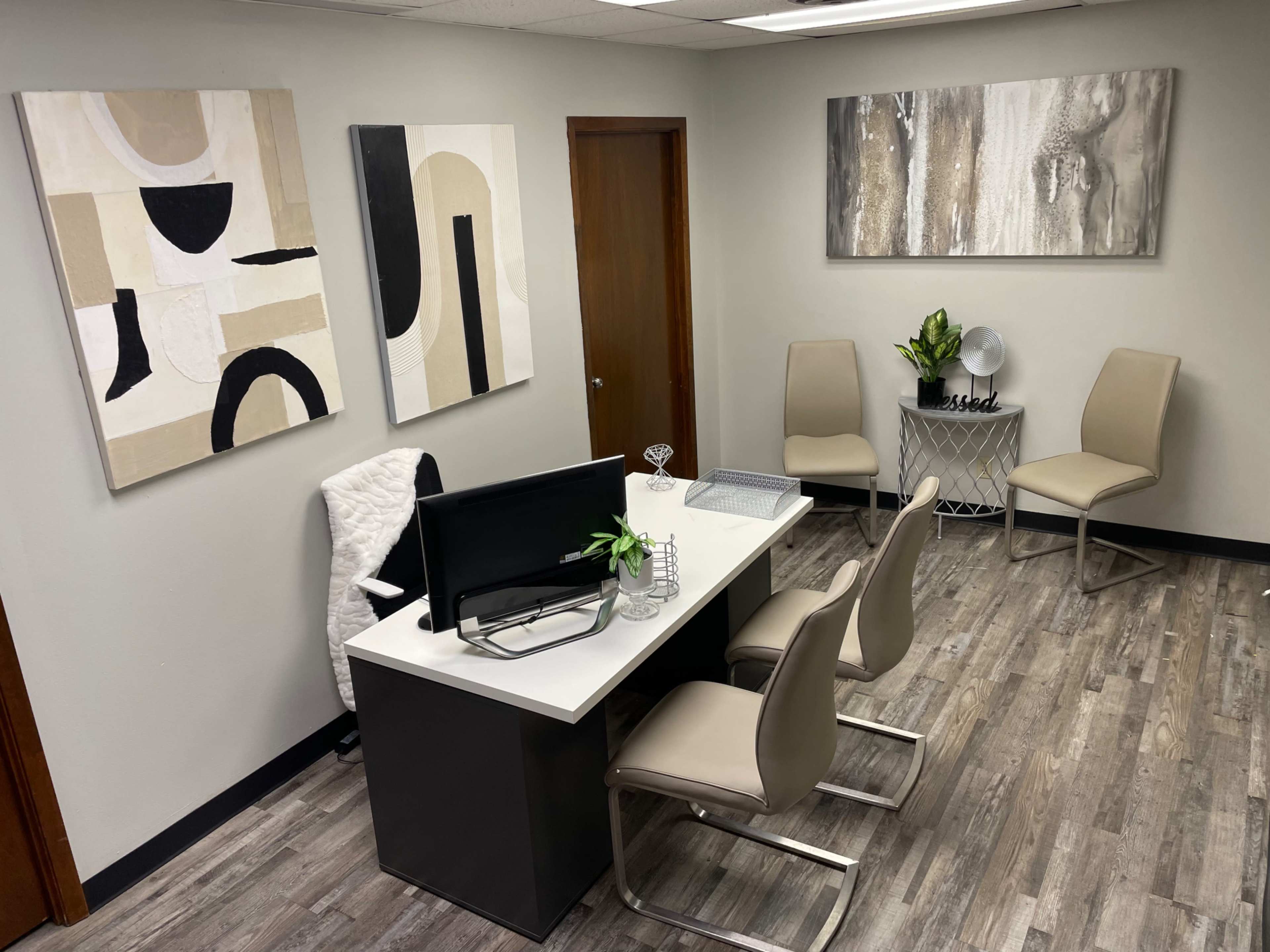 The image shows a modern office space featuring a desk with a computer, two chairs, and abstract artwork on the walls.