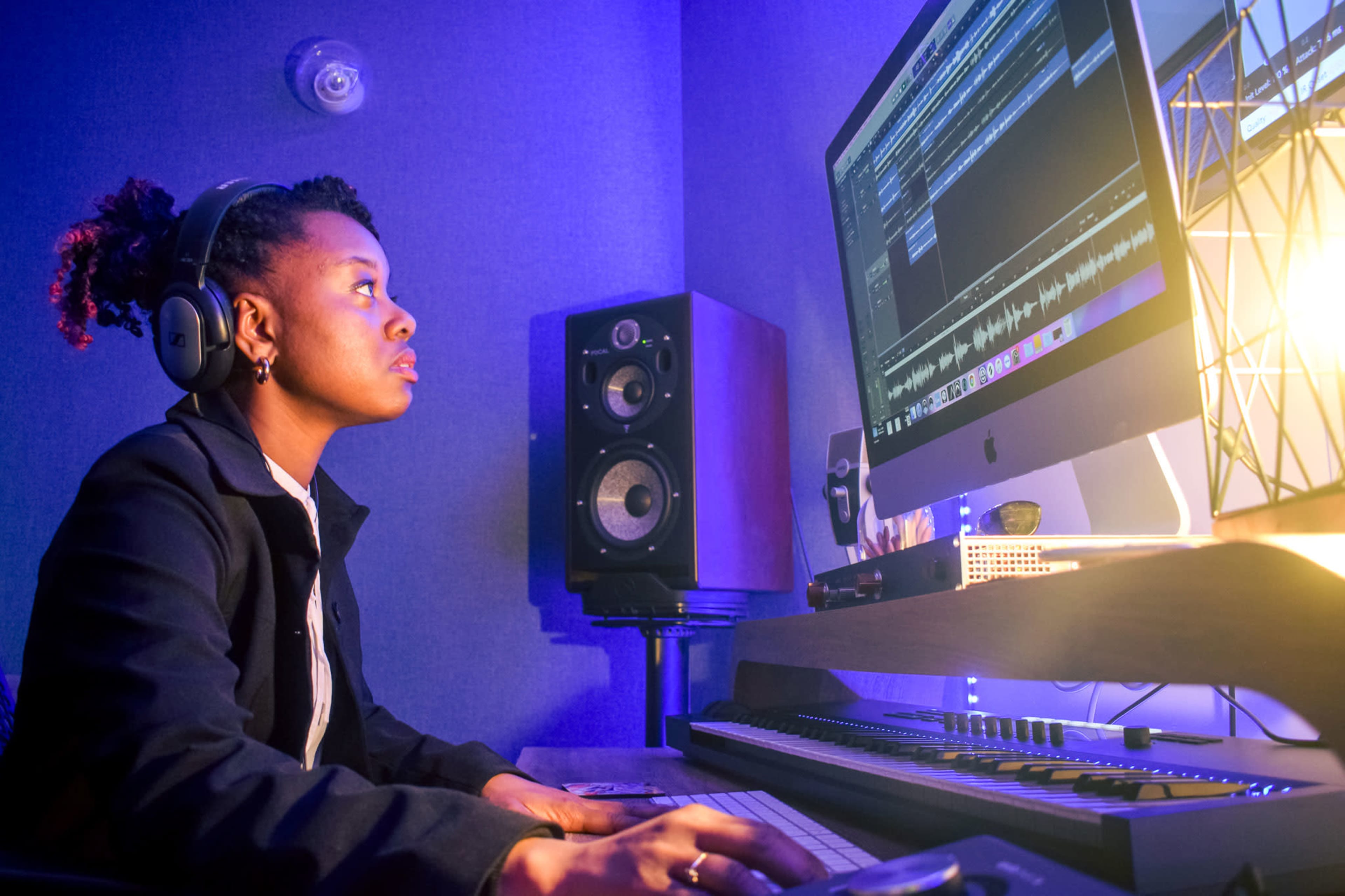 A person wearing headphones is focused on a computer screen while seated at a music production setup.