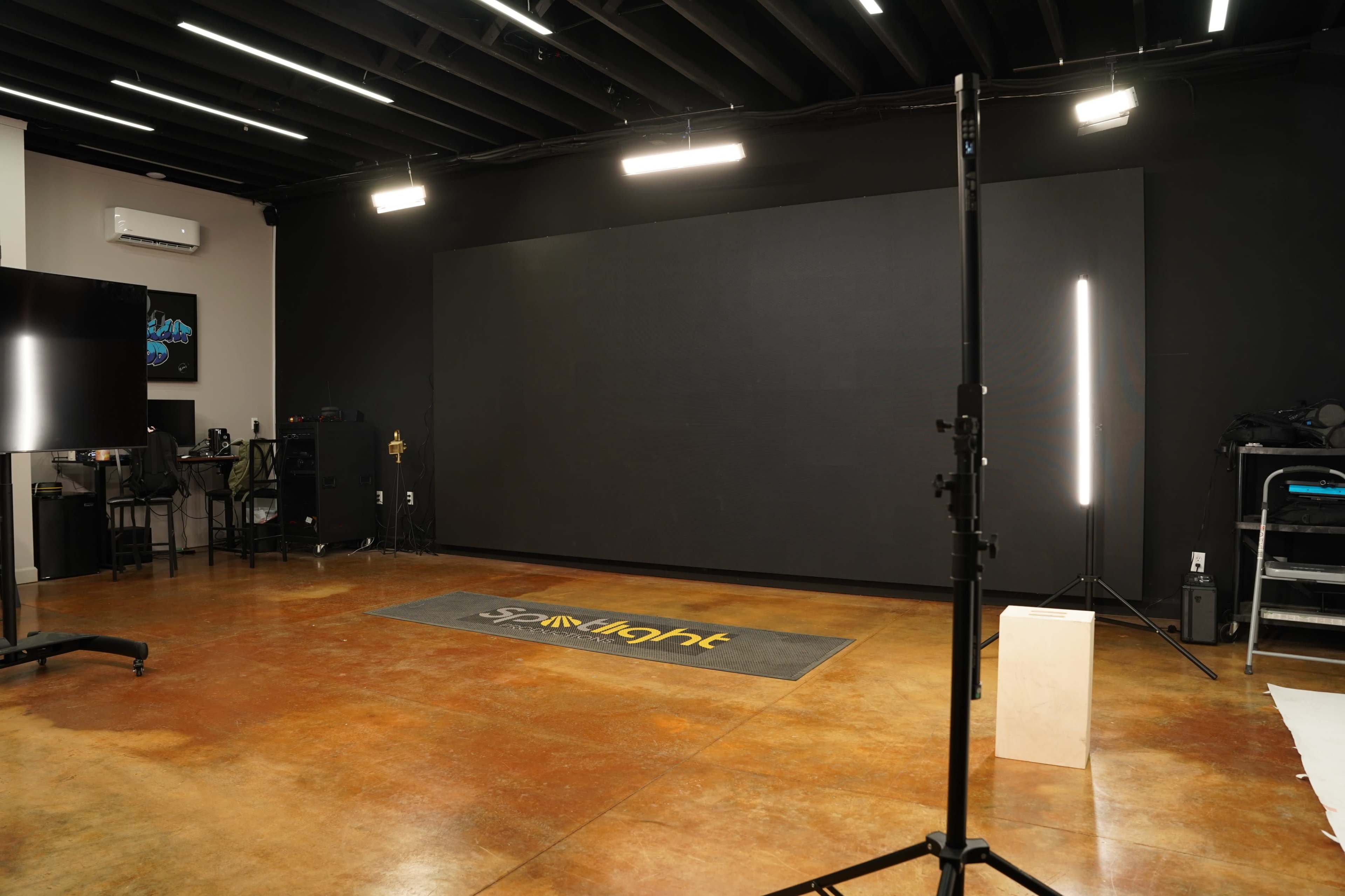 A spacious studio with a polished concrete floor, a large plain black backdrop, and various lighting equipment set up.