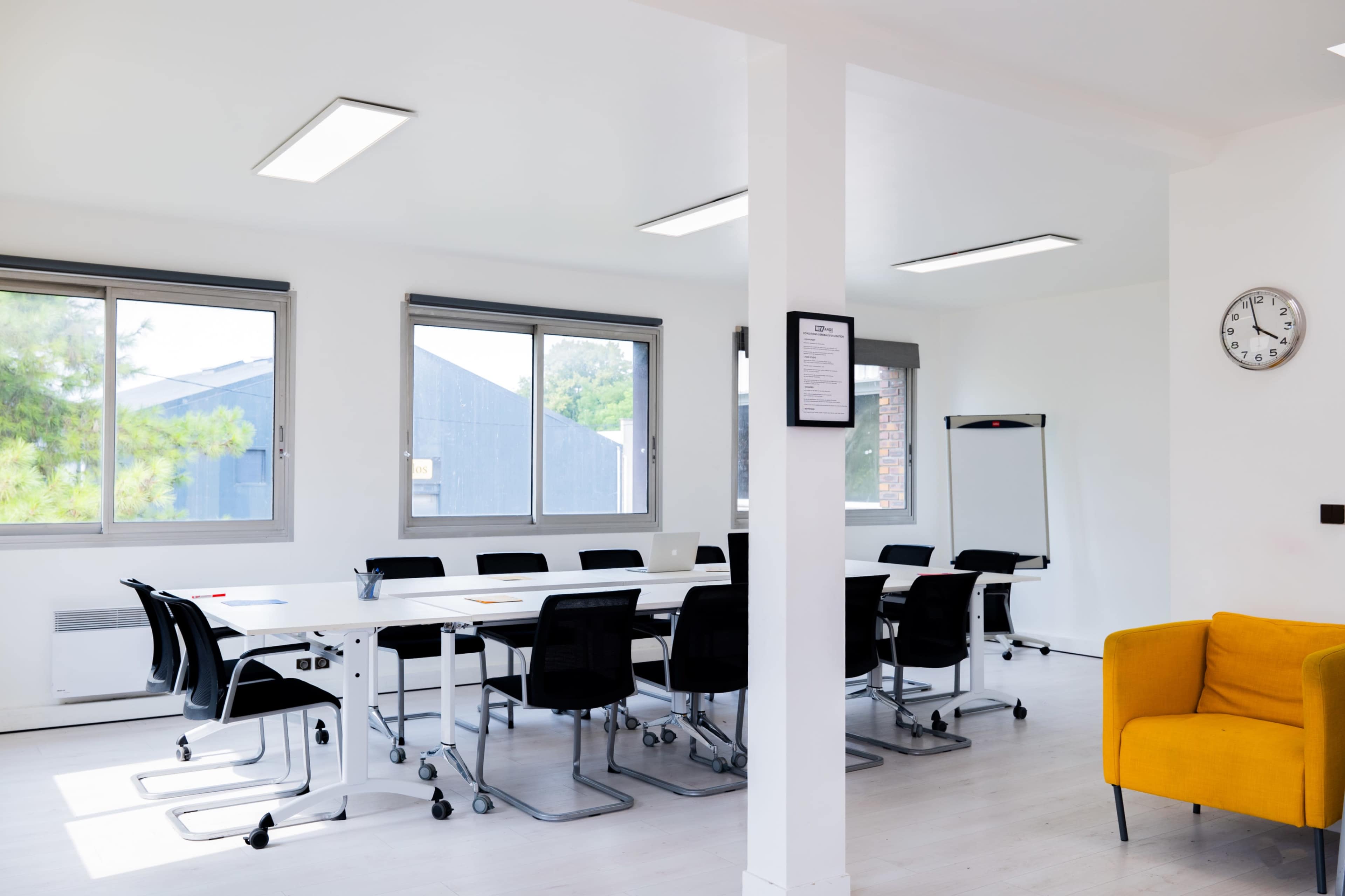 A bright meeting room furnished with a long table surrounded by black chairs, a whiteboard, and a yellow armchair.
