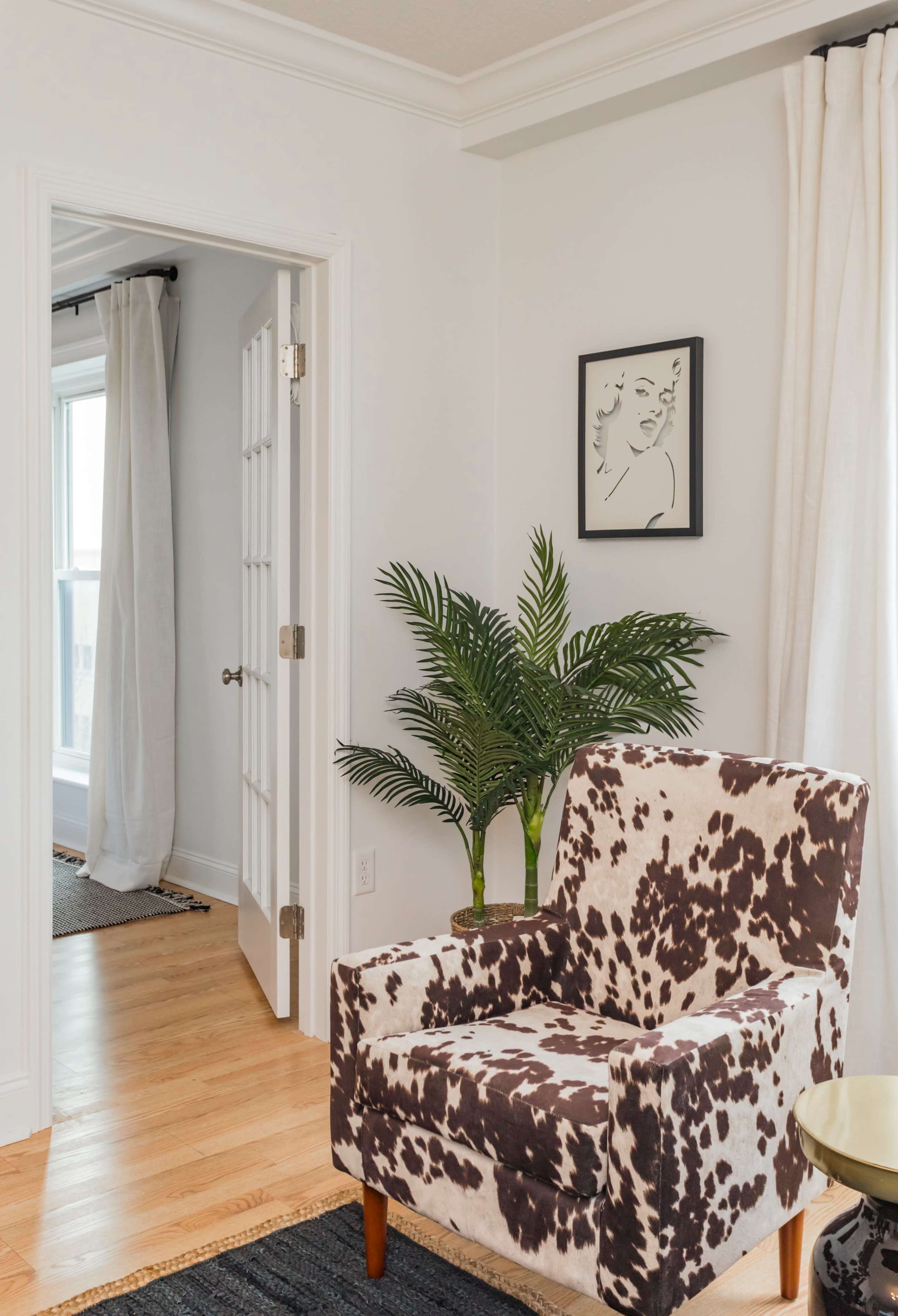 A room featuring a patterned armchair, a potted plant, and a doorway leading to another space.