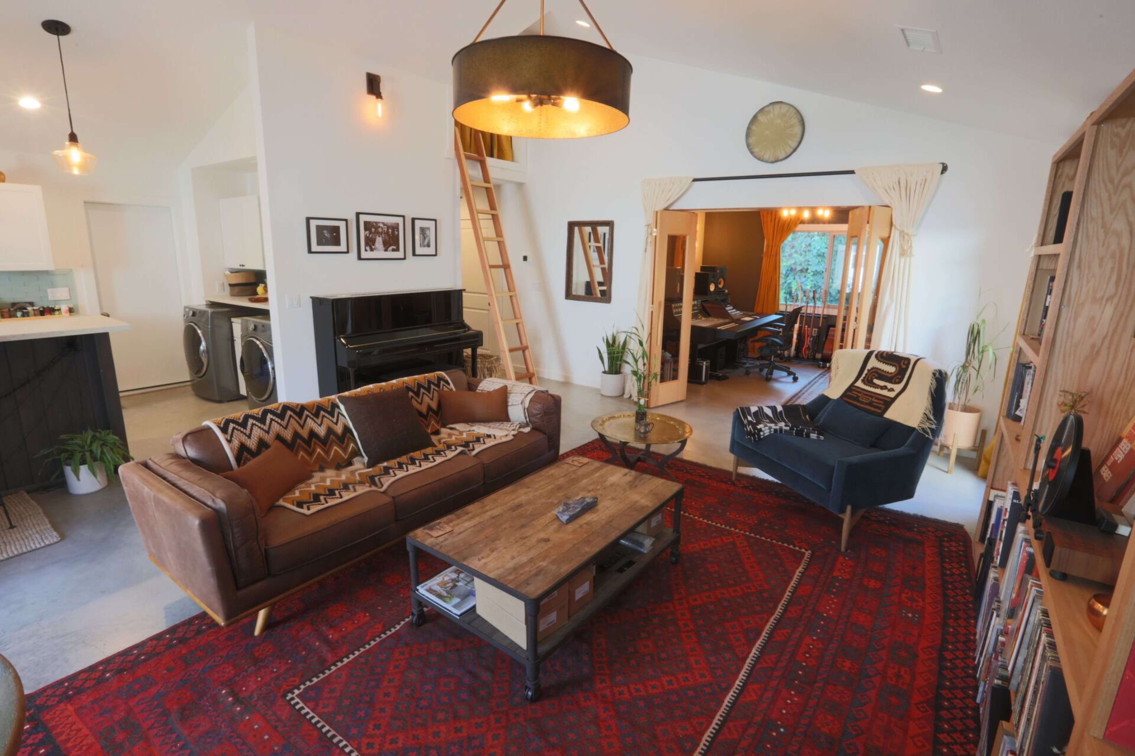 A cozy living room features a brown leather sofa, a wooden coffee table, and a patterned rug, with a piano and open doorway leading to a music area.