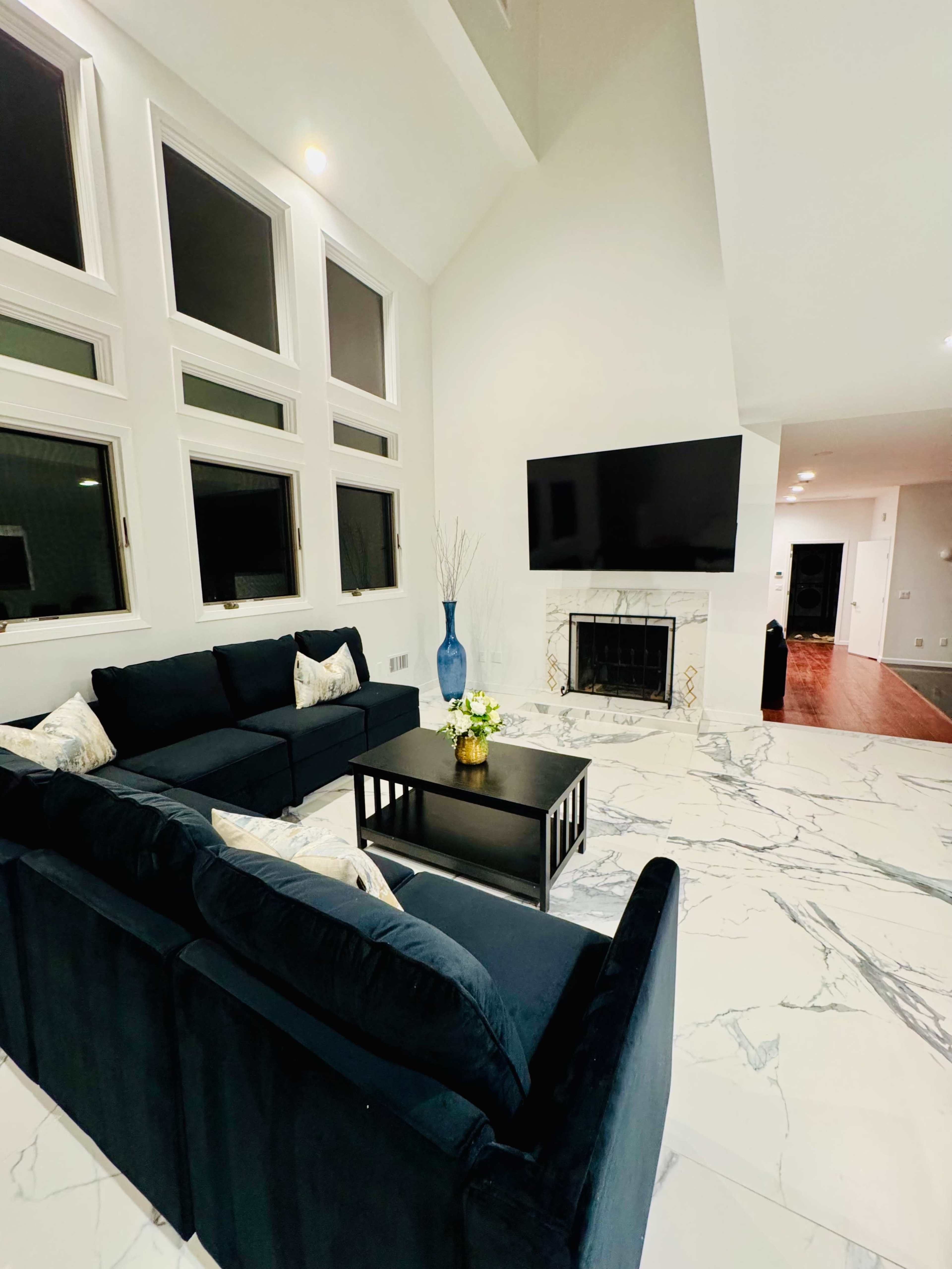The image shows a modern living room with a navy blue sectional sofa, a coffee table, and a large flat-screen TV mounted on the wall, surrounded by white marble flooring.