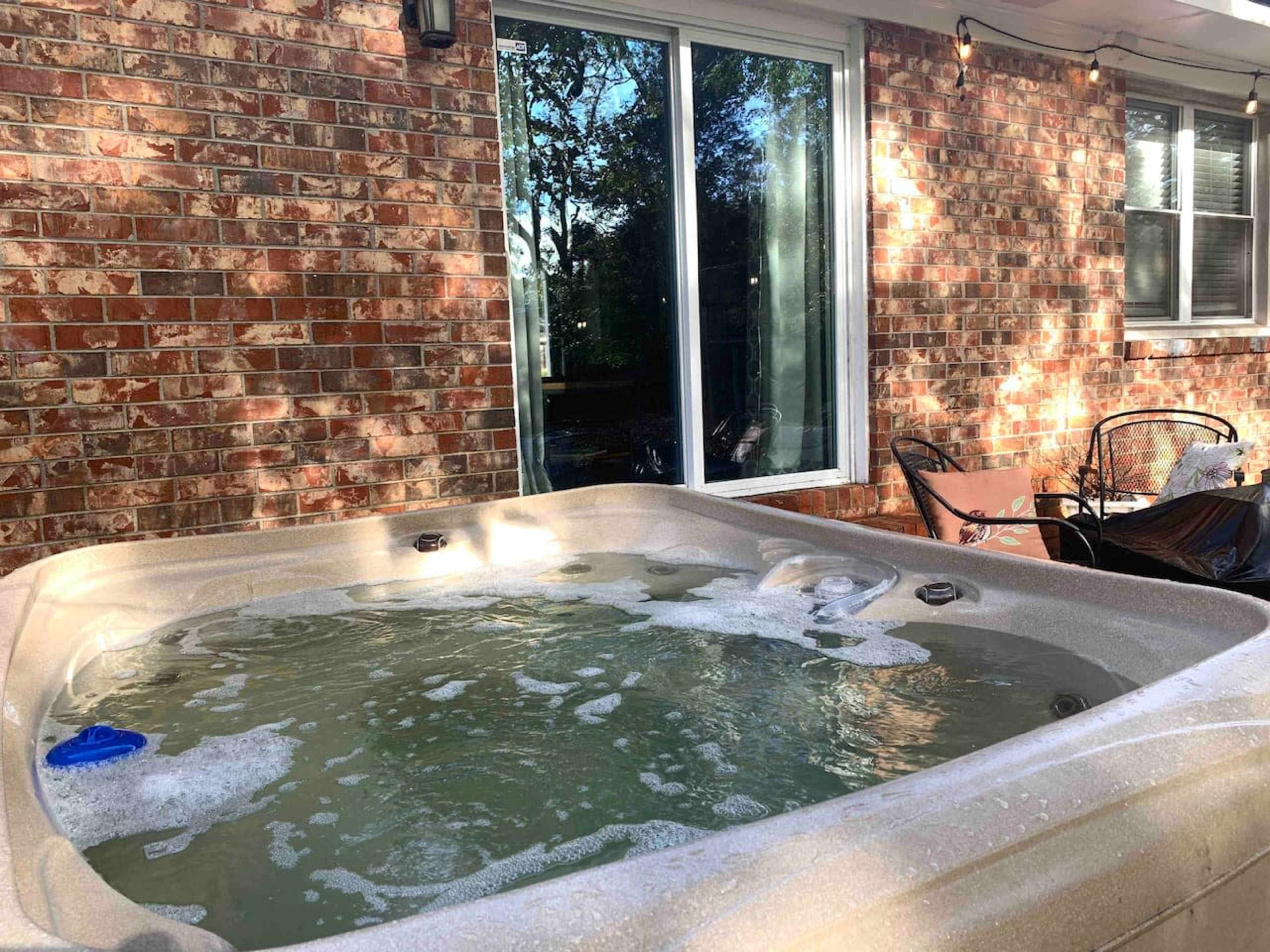 A hot tub with bubbles is positioned next to a brick wall and a large glass sliding door.