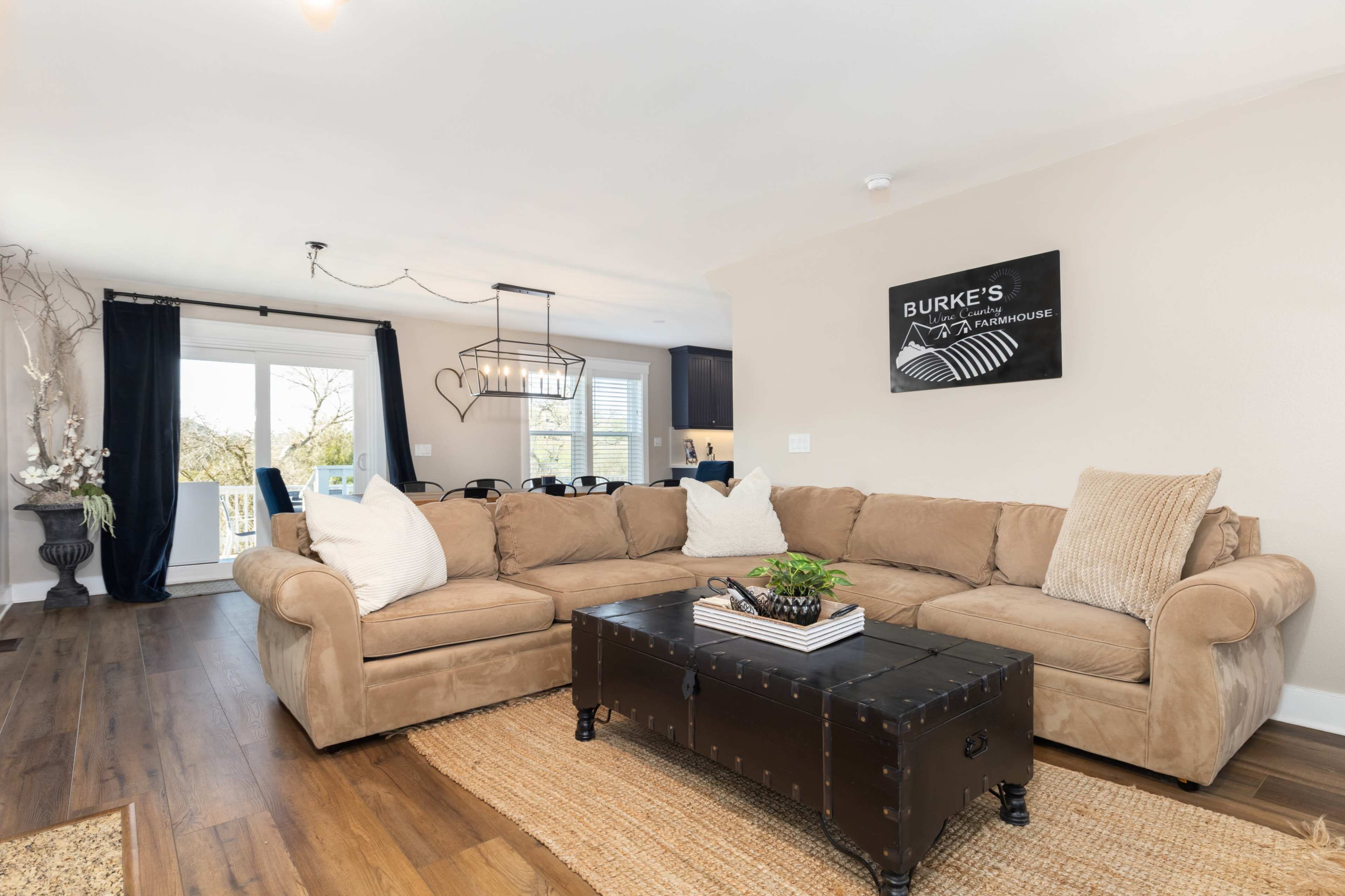 A comfortable living room with a large beige sectional sofa, a dark coffee table, and a dining area visible in the background.
