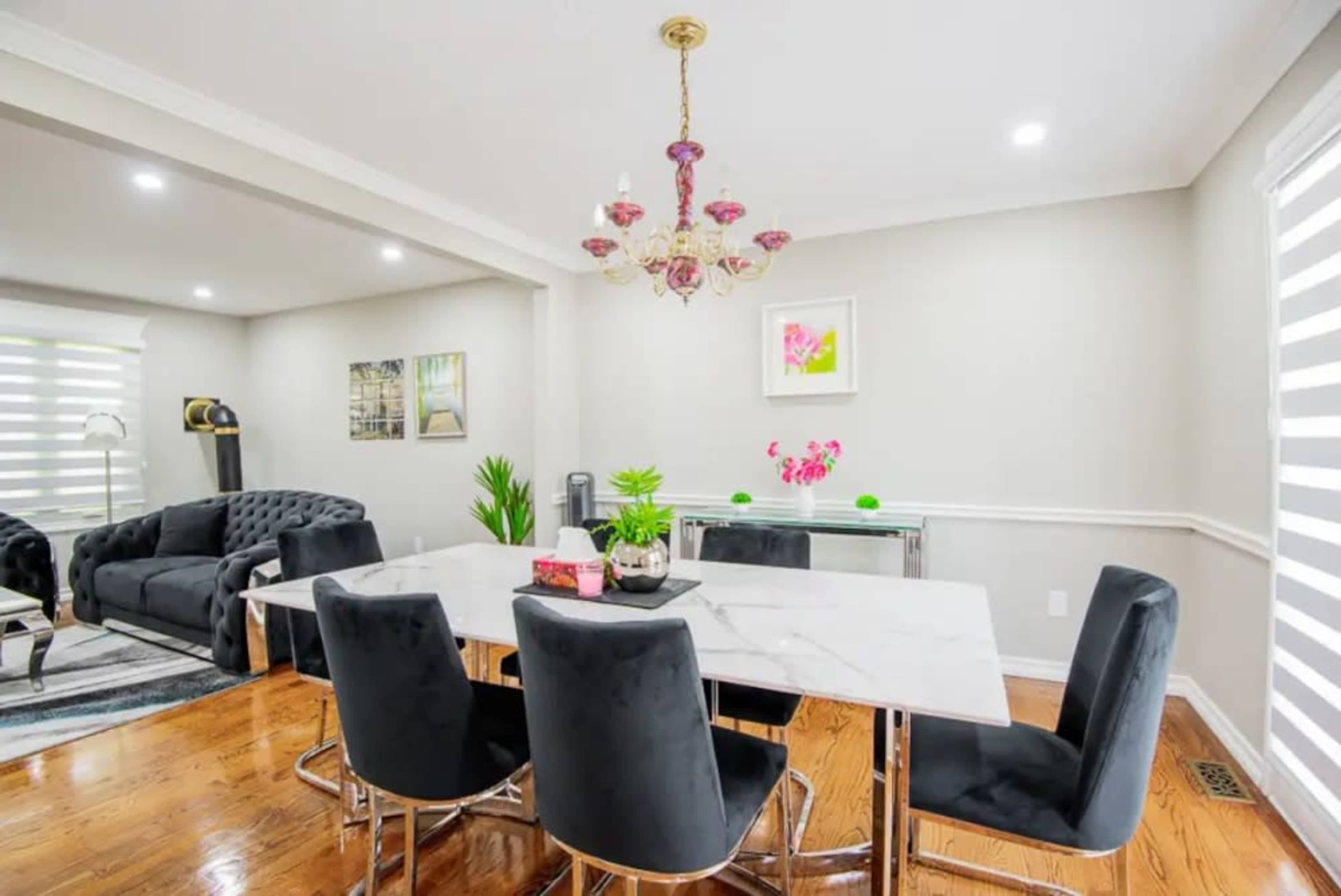 A modern dining area featuring a marble table surrounded by black chairs, with a chandelier overhead and light-colored walls.