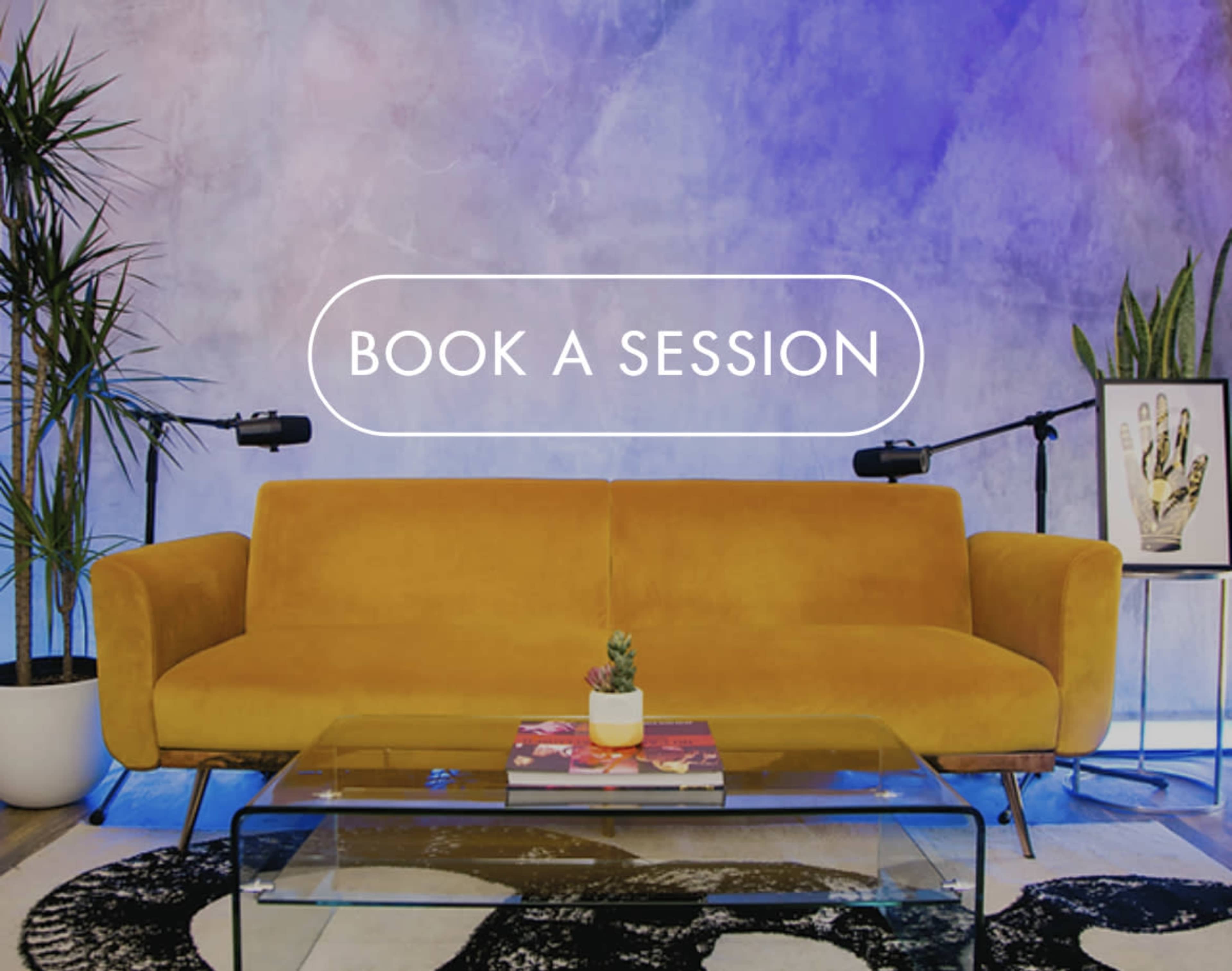 A yellow couch sits in front of a colorful mural, with a glass coffee table and a small plant on top.