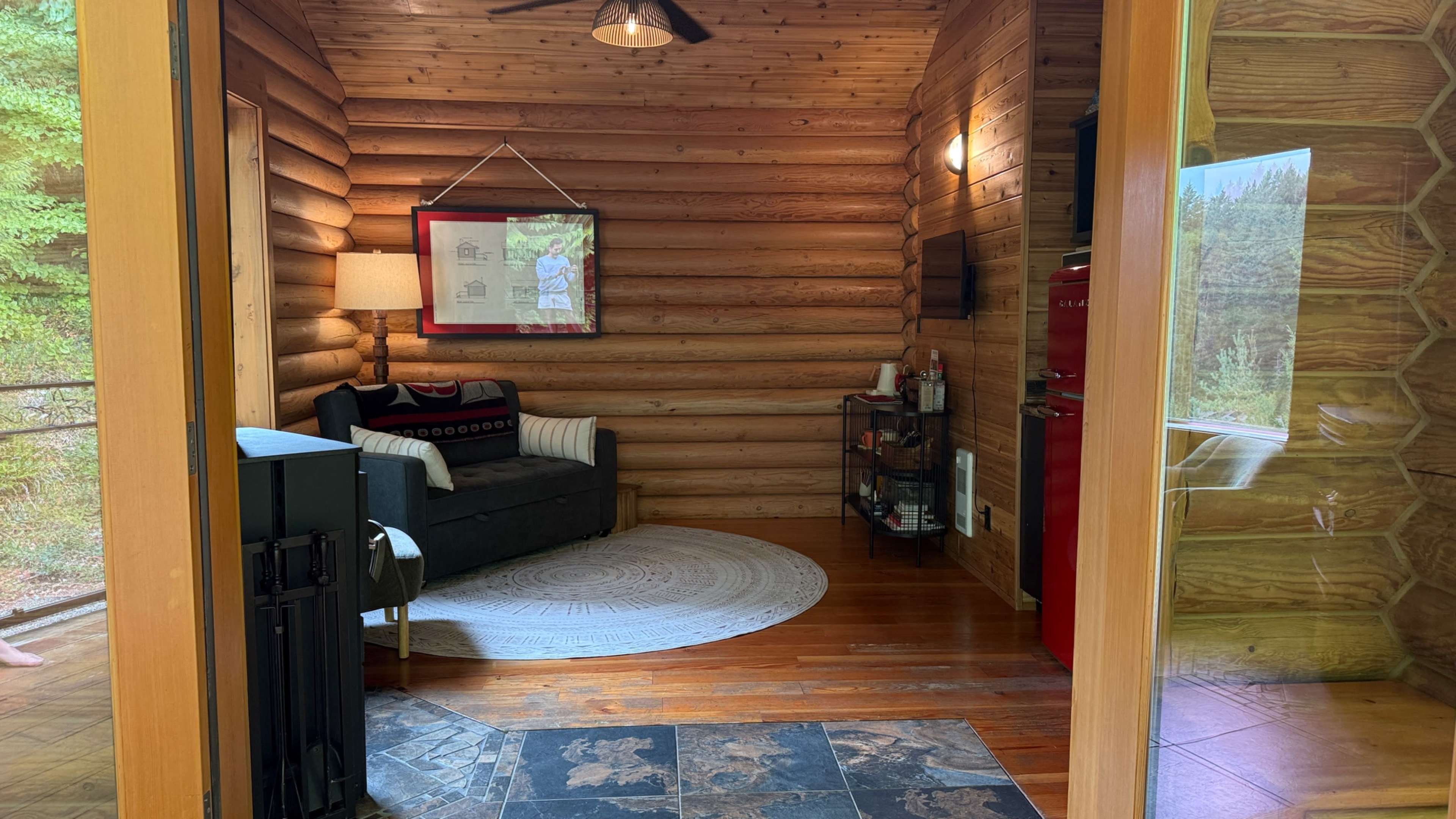 The image shows a wooden cabin interior with log walls, a sofa, a lamp, and a red refrigerator visible.