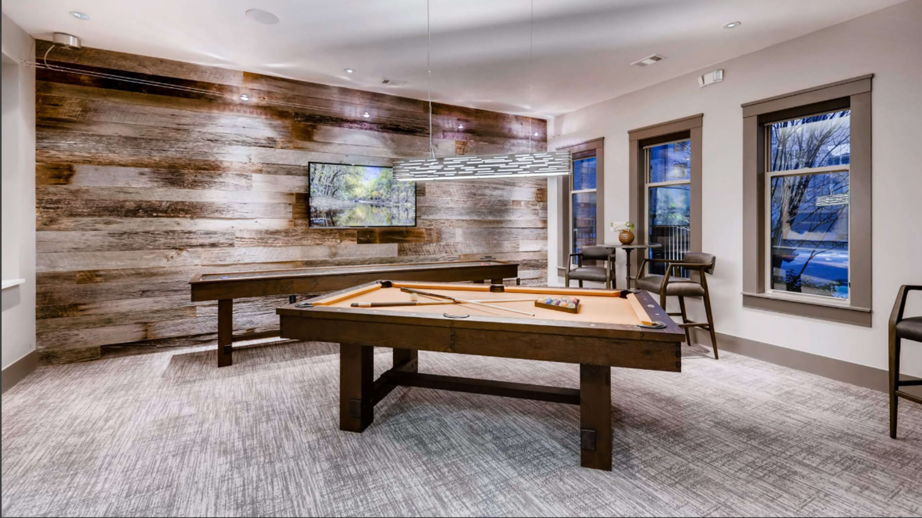 A game room with two pool tables, a modern light fixture, and large windows looking out onto a snowy landscape.