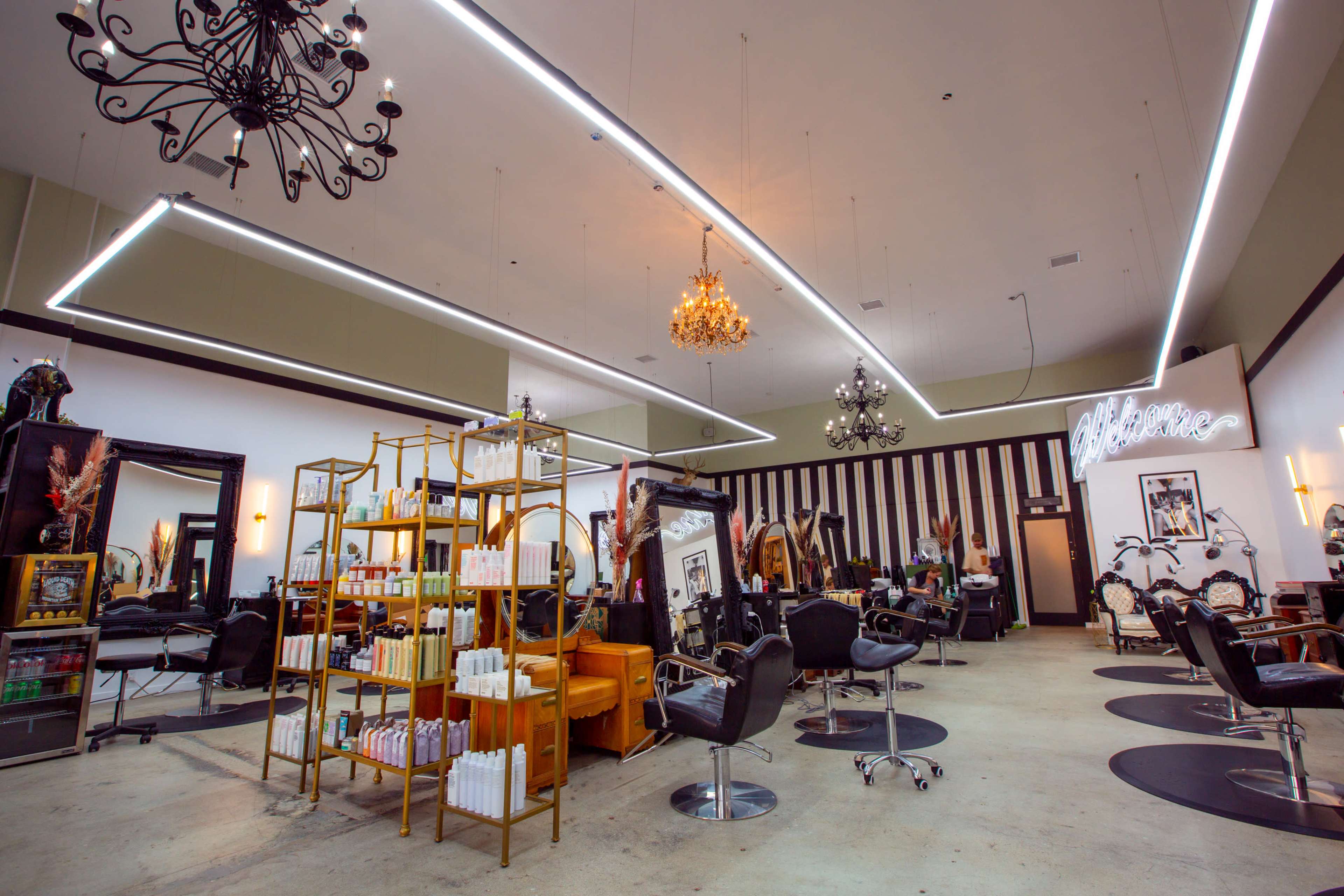 The interior of a modern hair salon featuring multiple styling stations, a product display shelf, and various lighting fixtures.