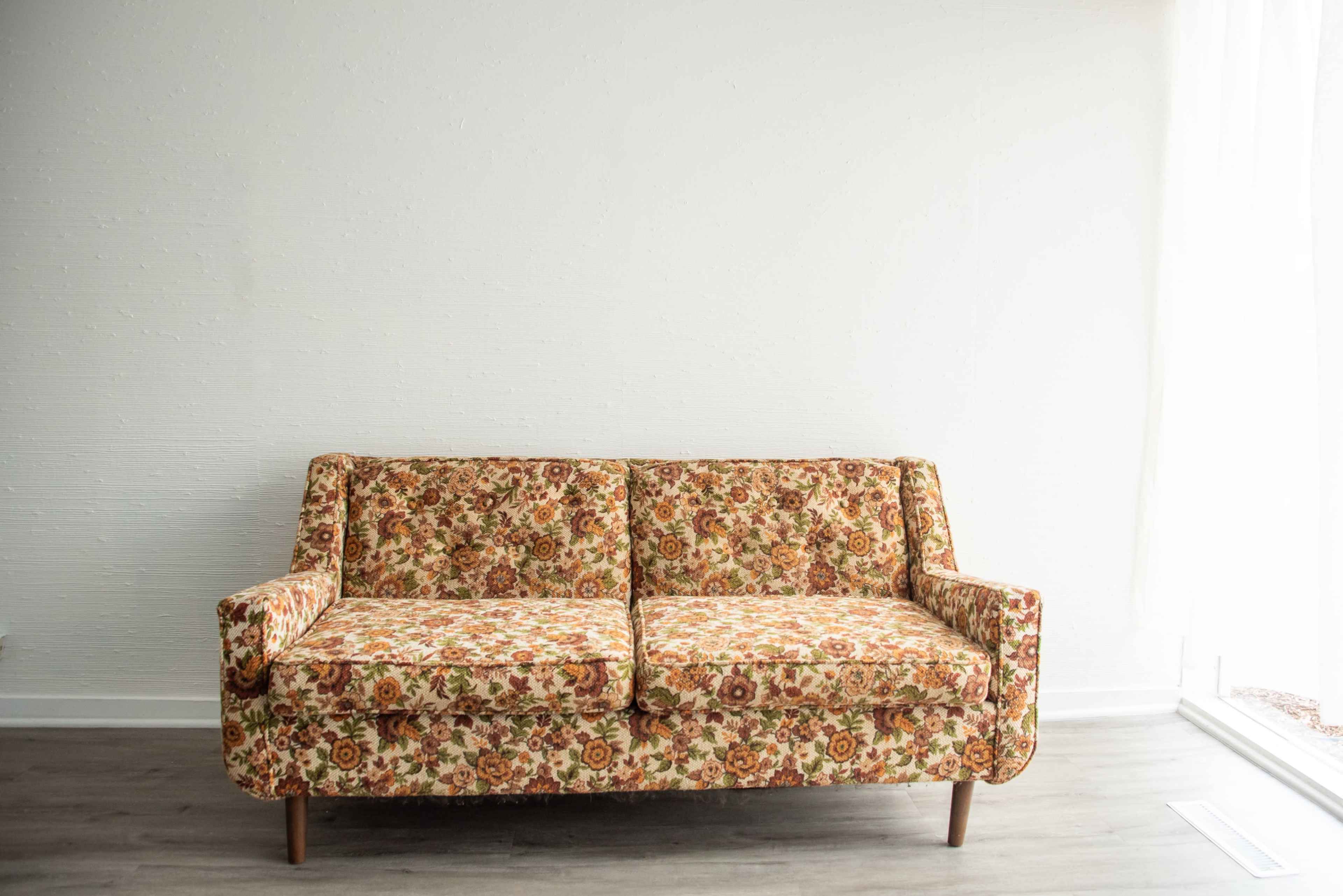A two-seater couch with a floral print upholstery is positioned against a plain white wall.