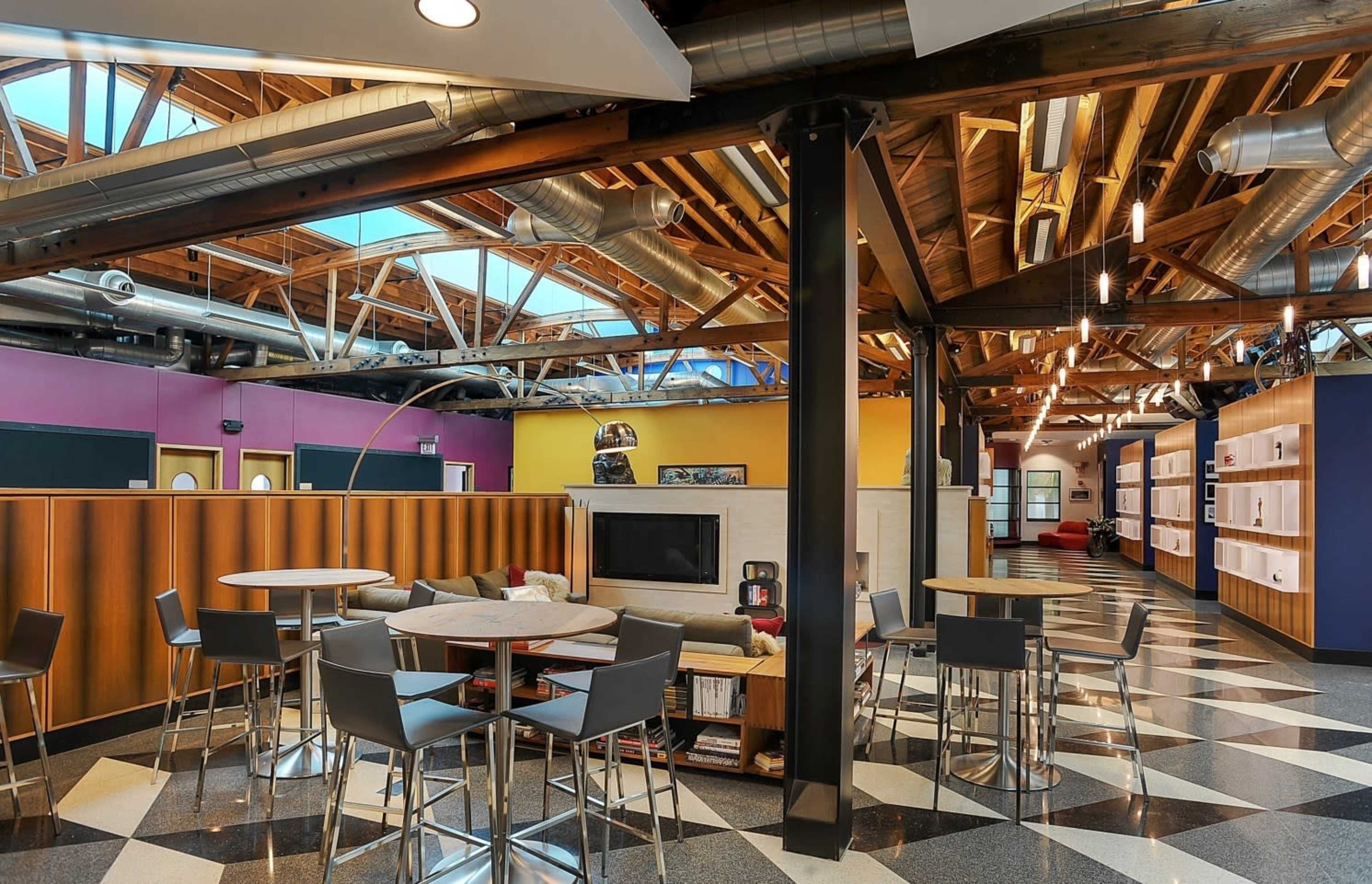 A modern office space featuring high ceilings with exposed beams, a mix of seating areas, and colorful walls.