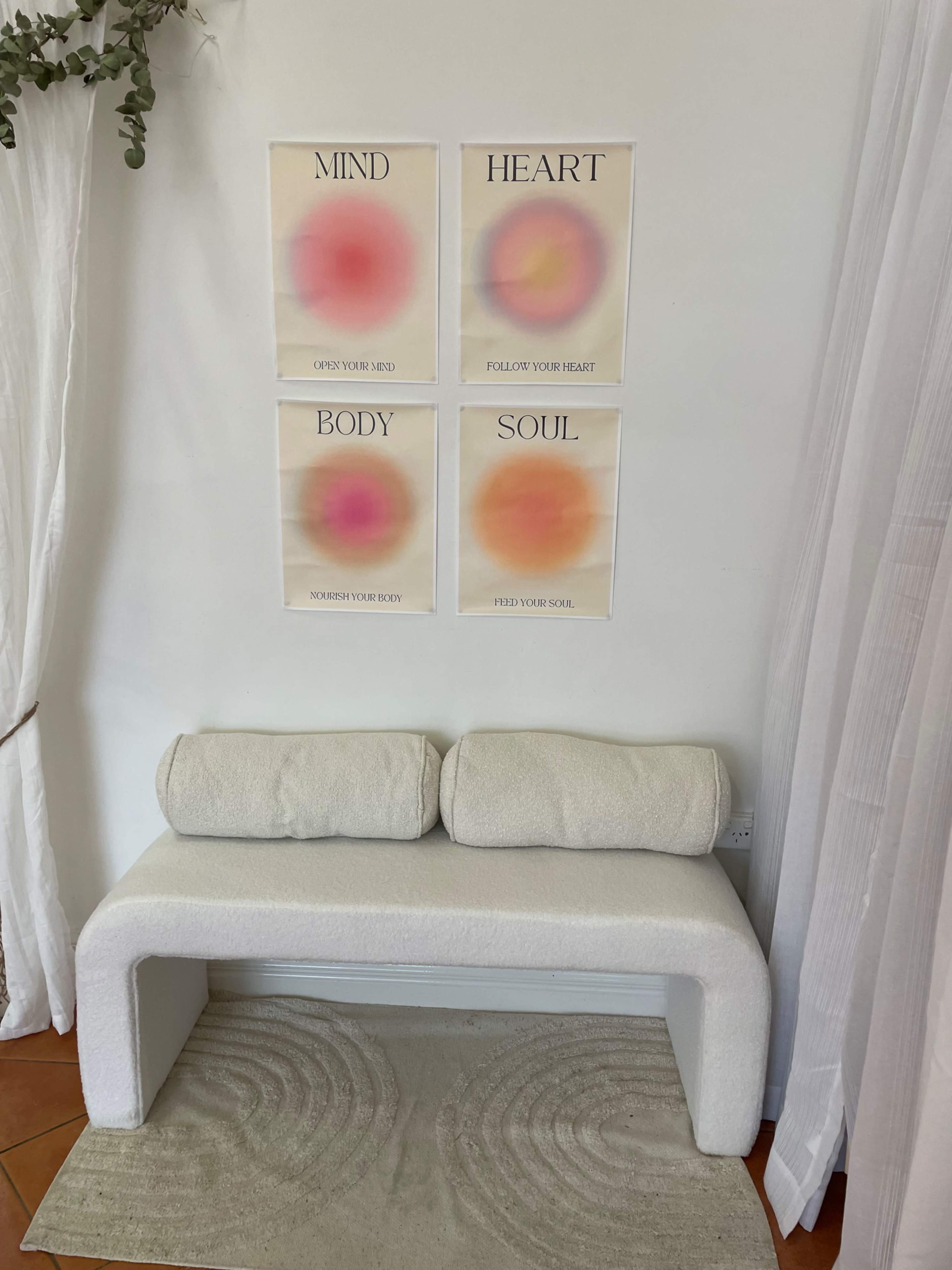 The image shows a minimalistic seating area with a curved white bench, a textured rug on the floor, and four colorful posters displaying the words "MIND," "HEART," "BODY," and "SOUL" on the wall.