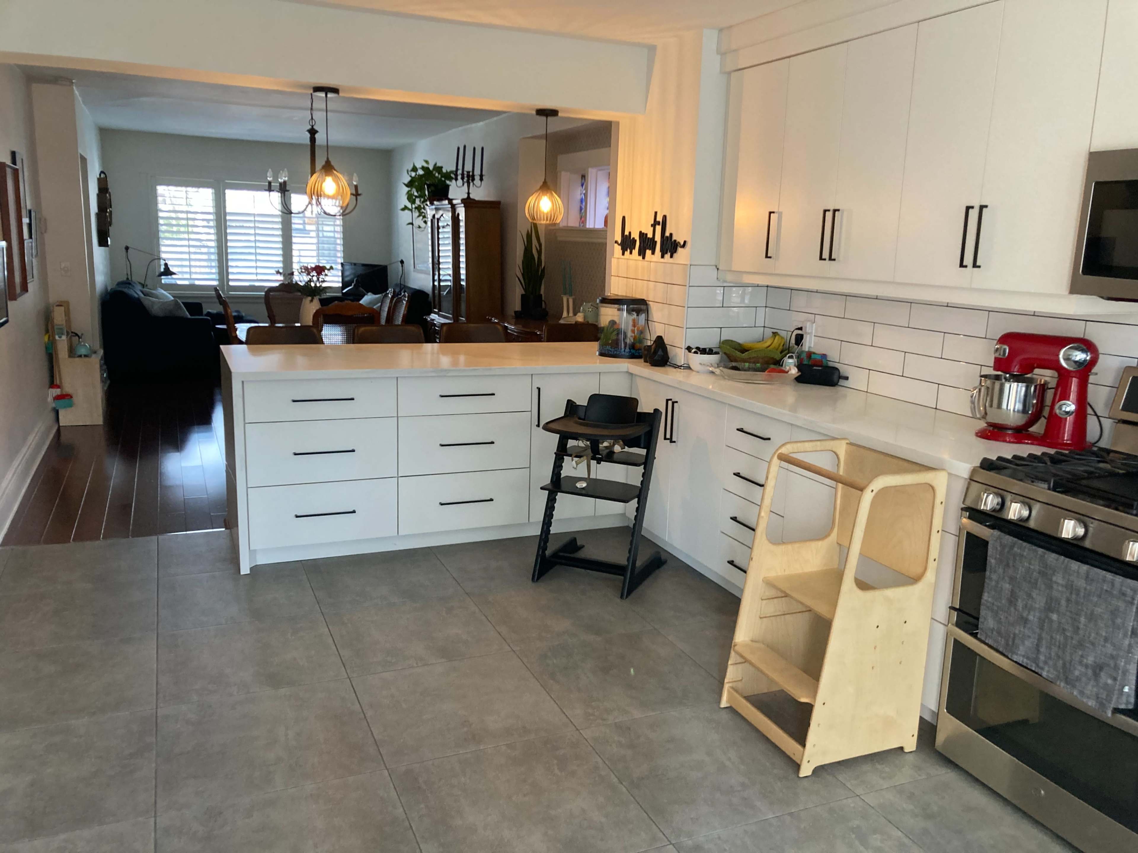 A modern kitchen features white cabinetry, a gas stove, and a wooden high chair next to a small step stool.
