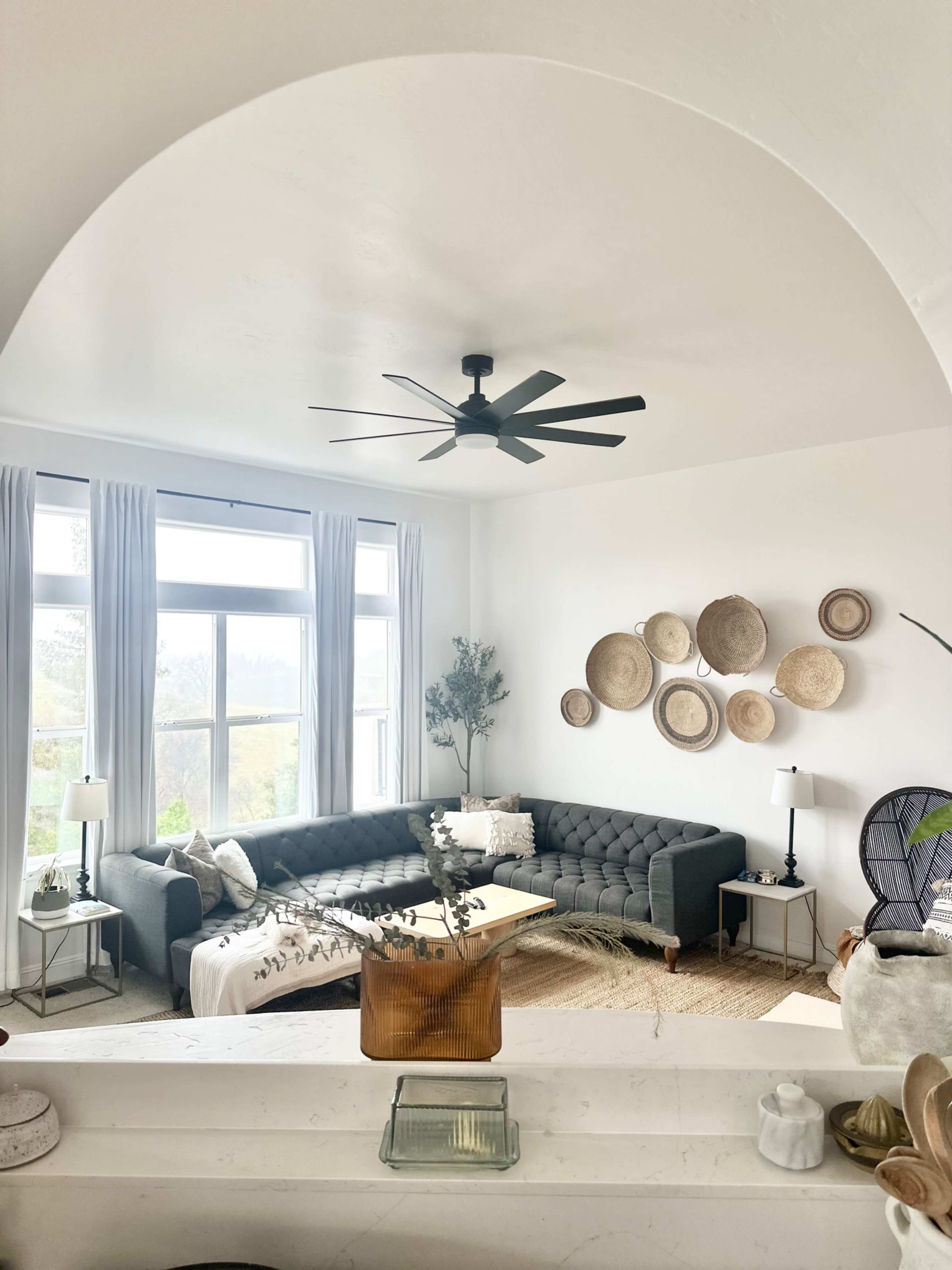 A modern living room features a sectional sofa, circular wall decor, and large windows allowing natural light.