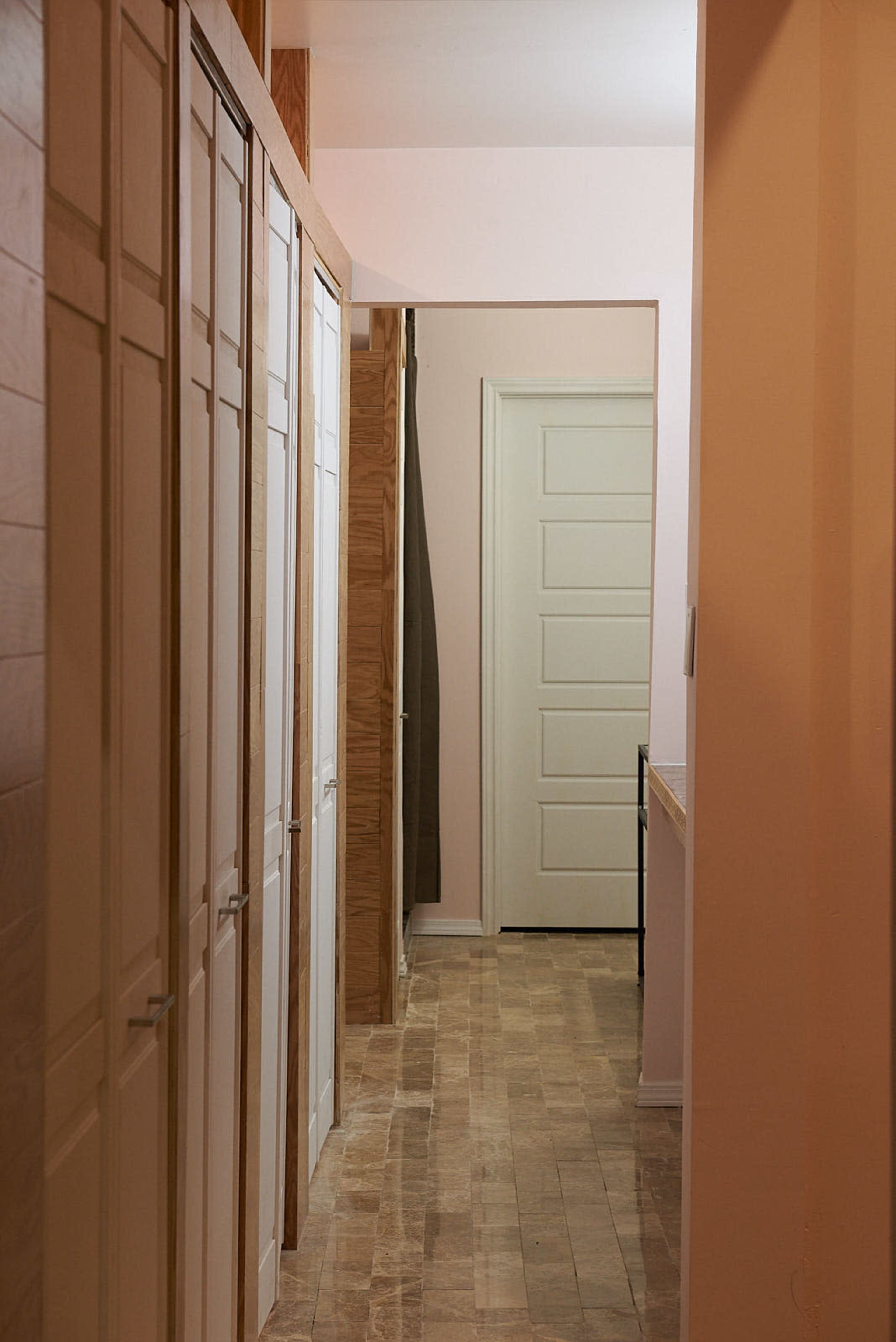 A narrow hallway features white cabinets on one side and leads to a doorway at the end.