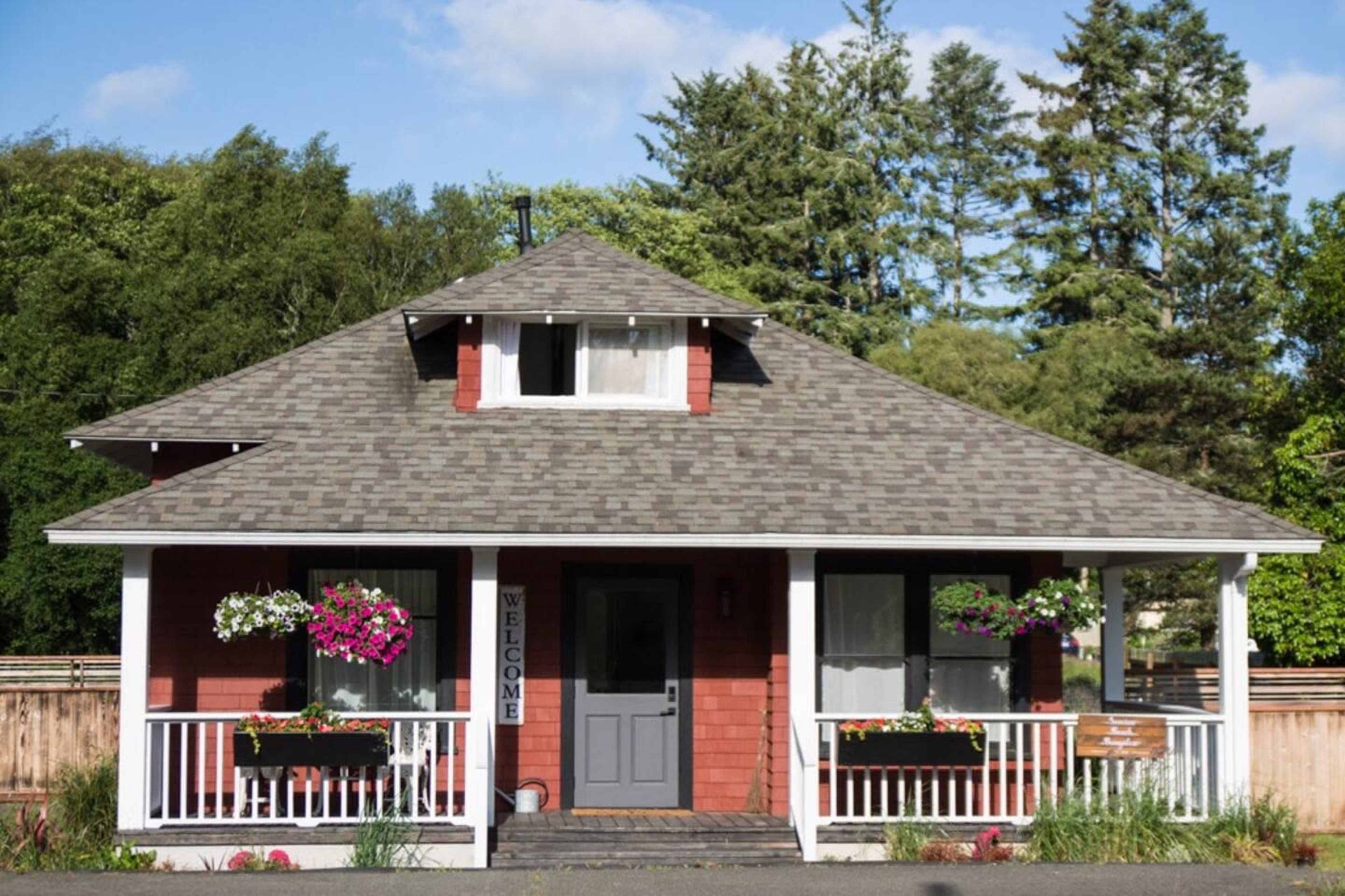 A red and white house with a gabled roof and a welcoming front porch is surrounded by greenery.