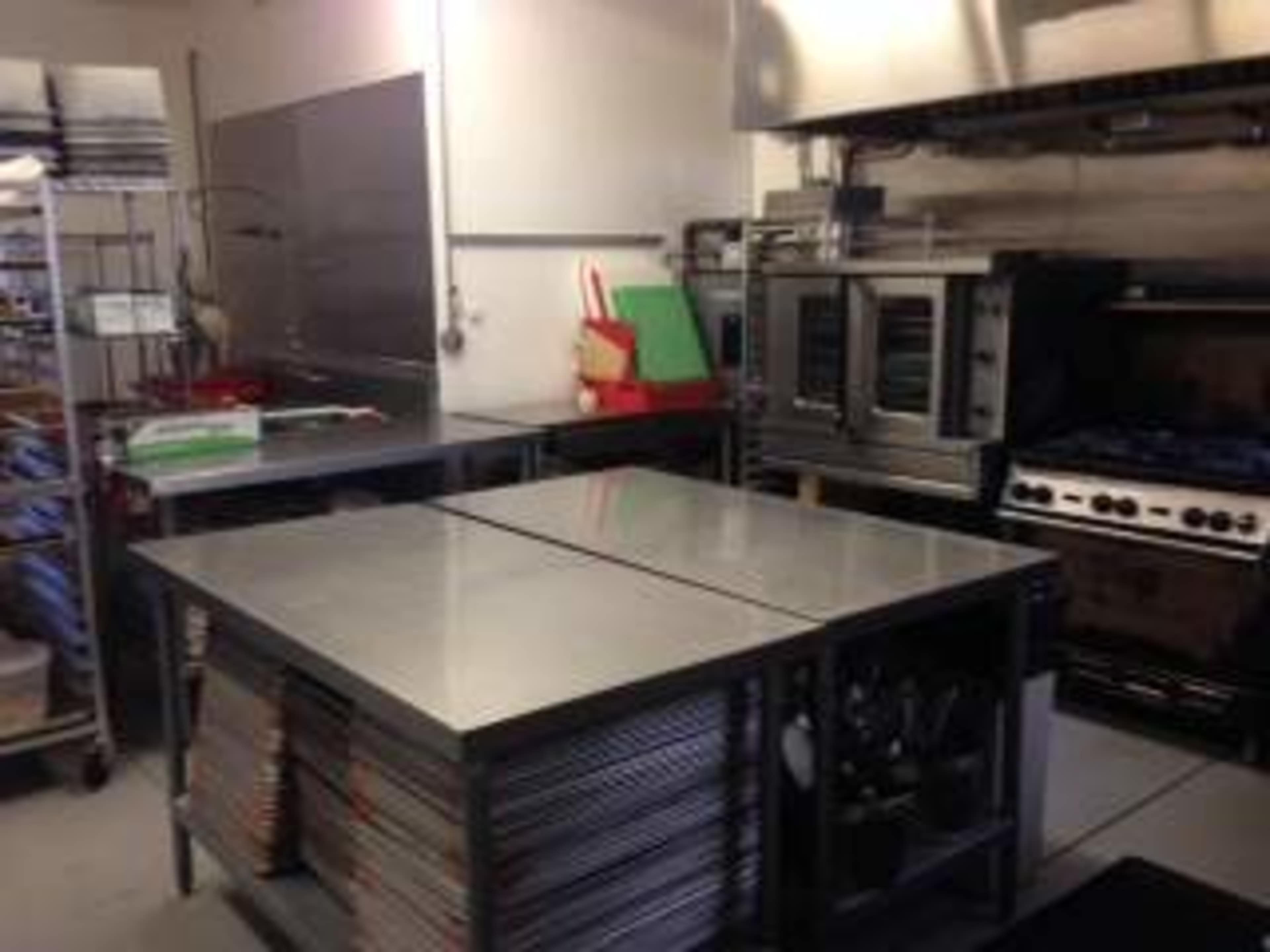 A commercial kitchen with stainless steel countertops, cooking equipment, and shelving.