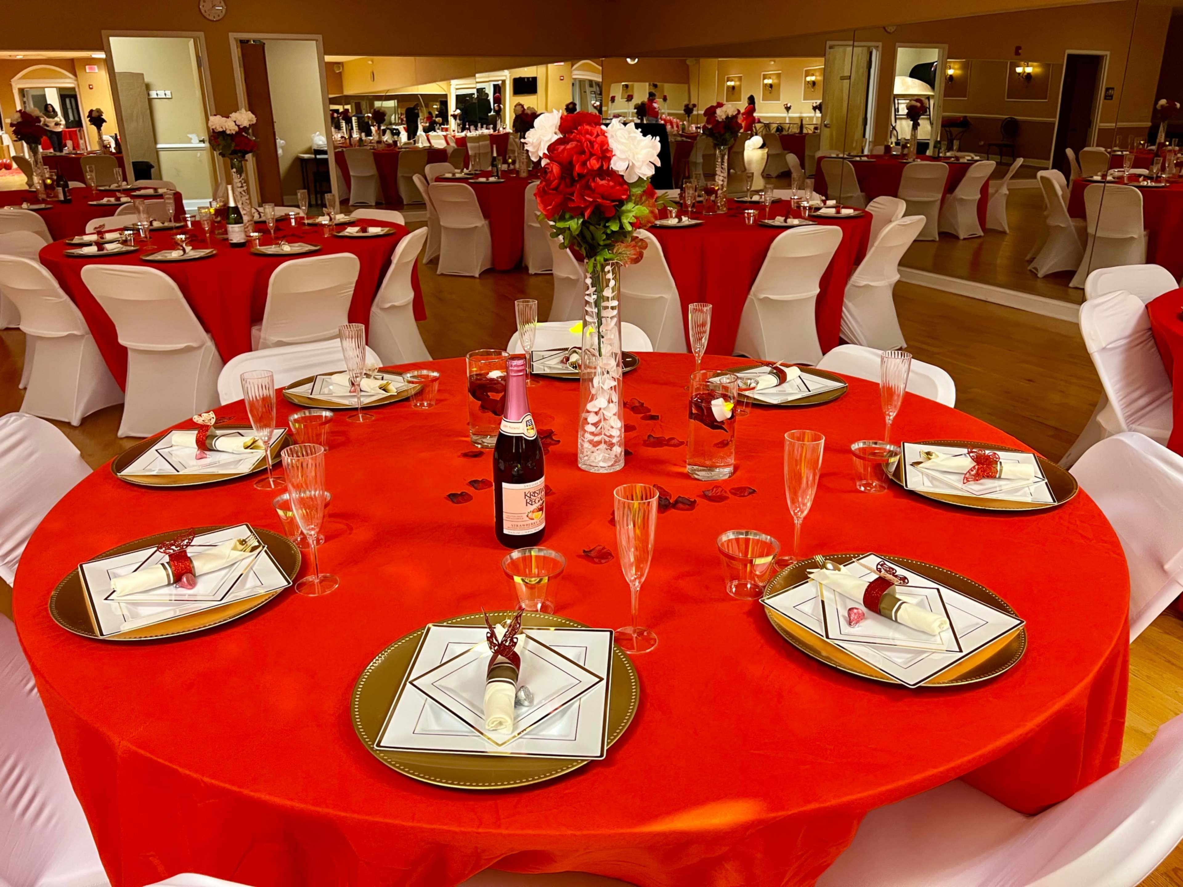 A dining setup features red tablecloths with elegant place settings, decorative centerpieces of flowers, and champagne flutes.
