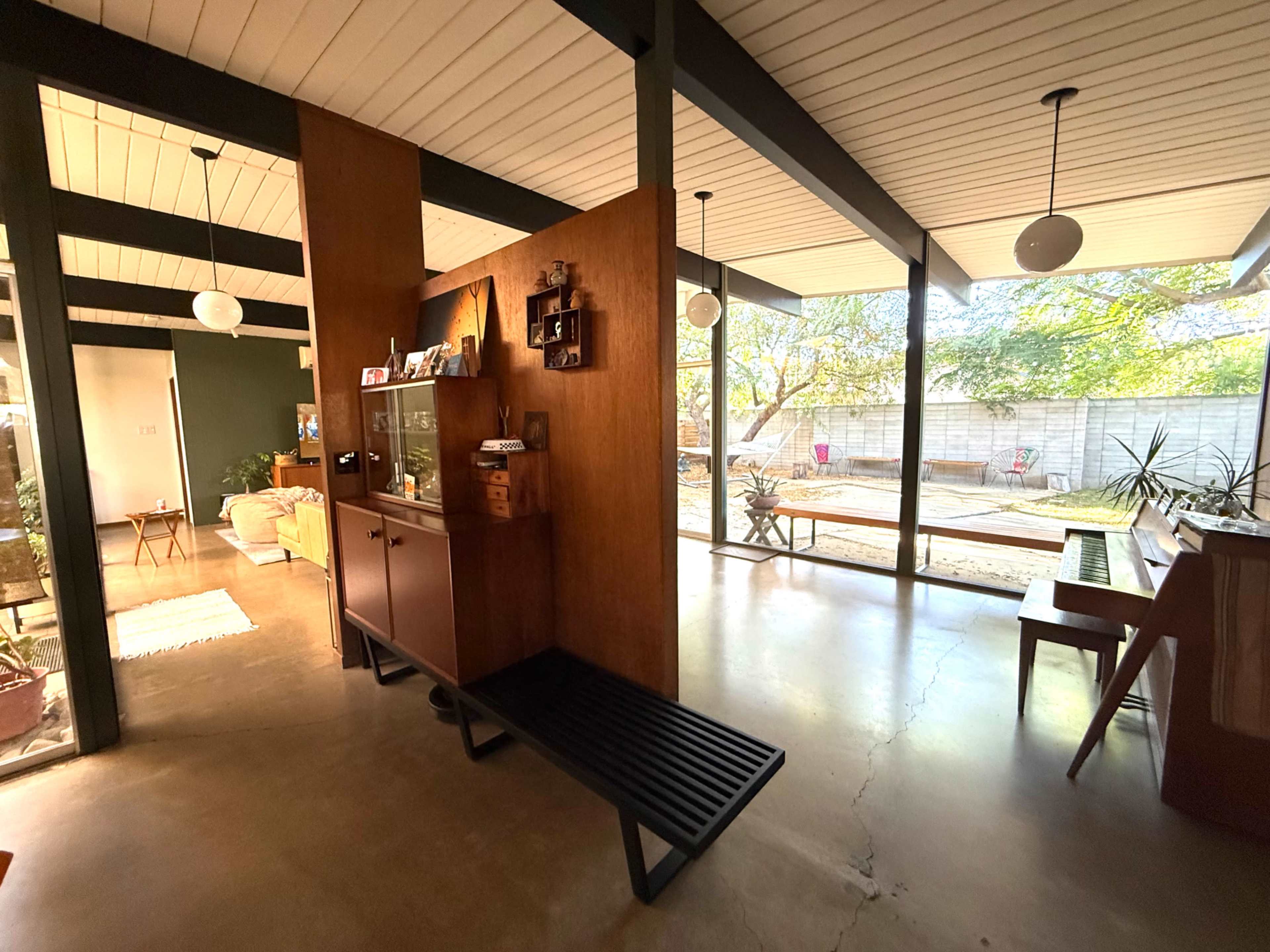The image shows a modern interior space with a wooden partition separating the living area from a garden view, featuring minimalist furniture and natural light coming through large windows.