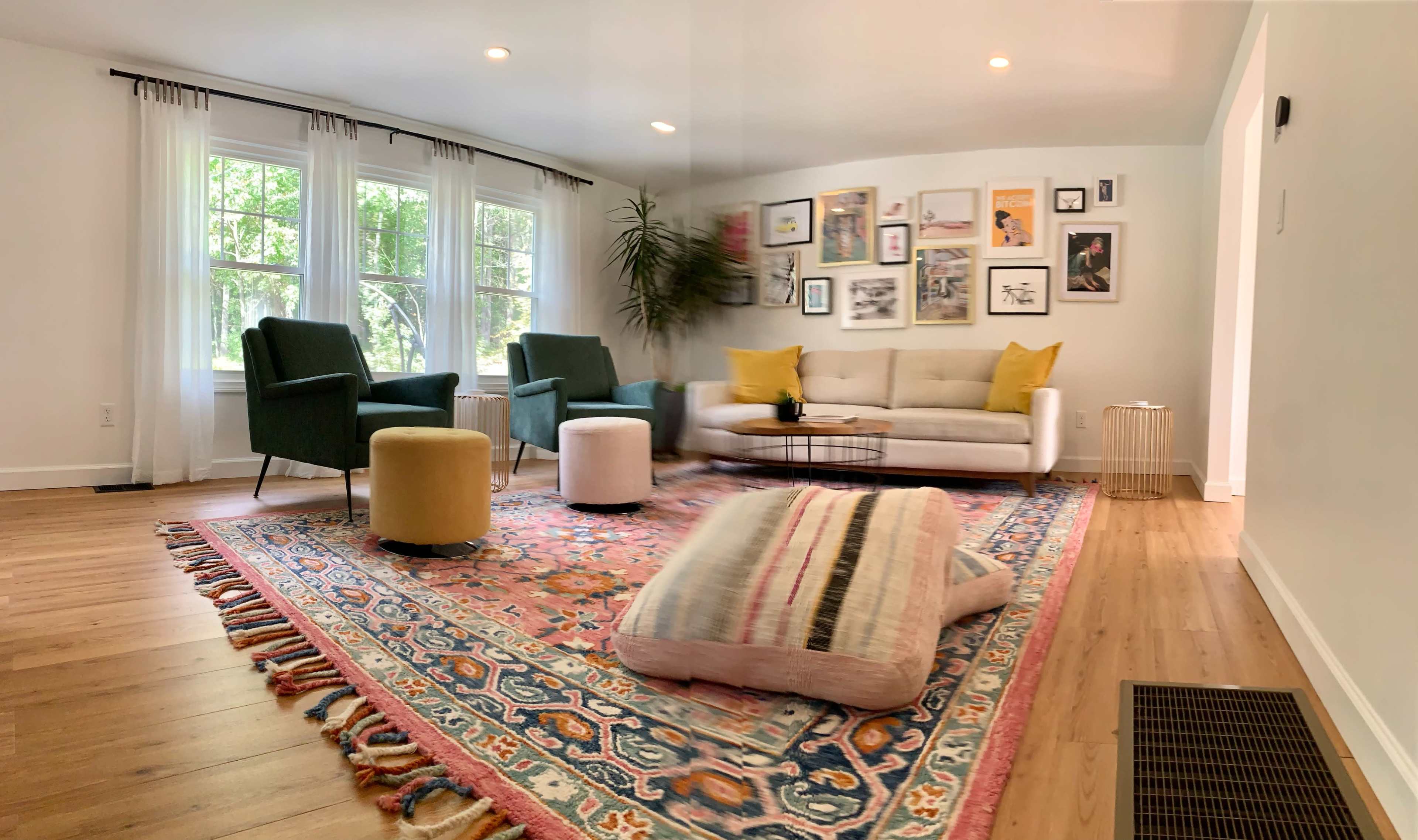 A bright living room with a large area rug, a beige sofa, green armchairs, and a gallery wall of framed pictures.