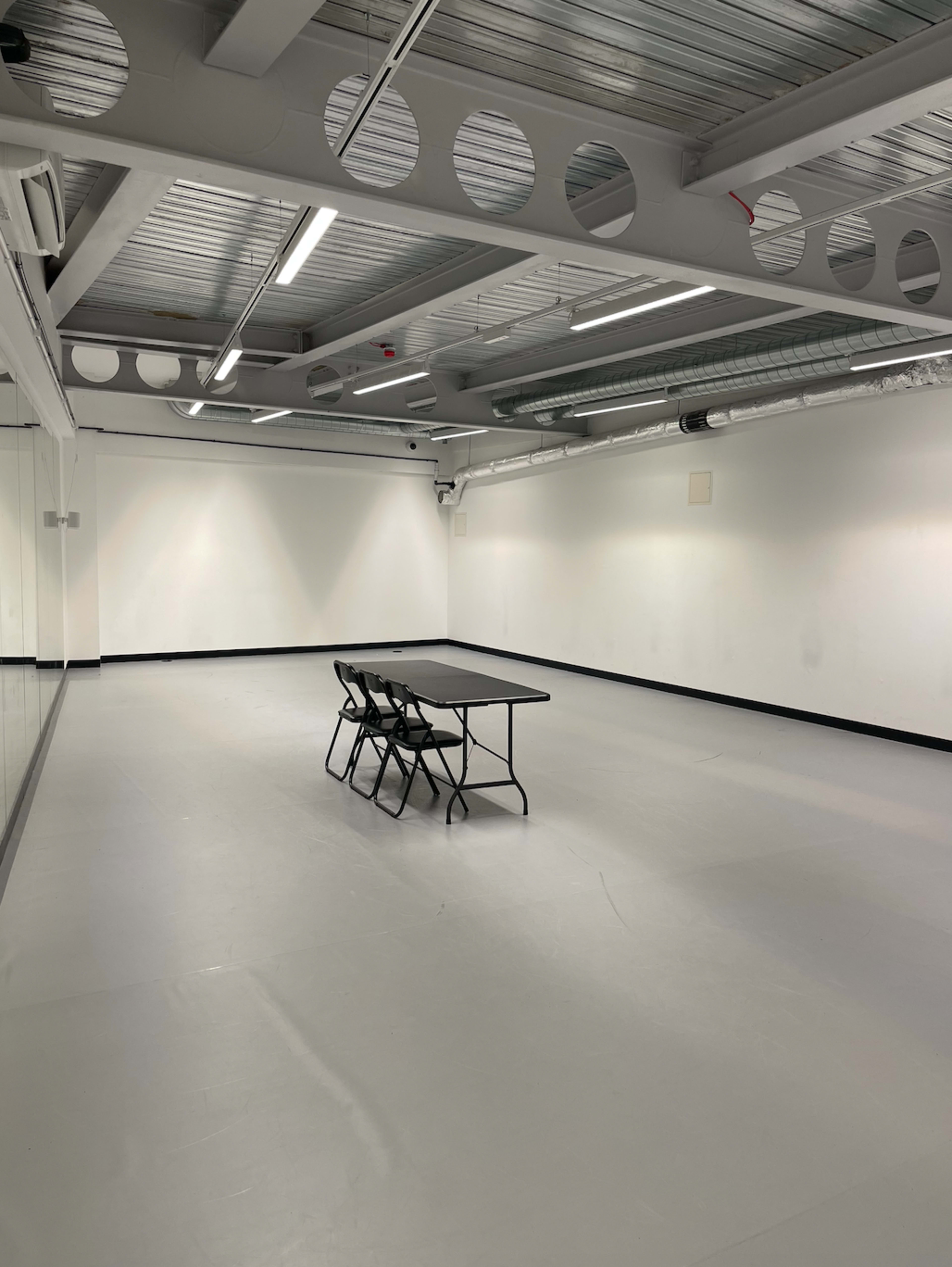 A minimalistic room features a table with four chairs arranged around it on a gray floor.