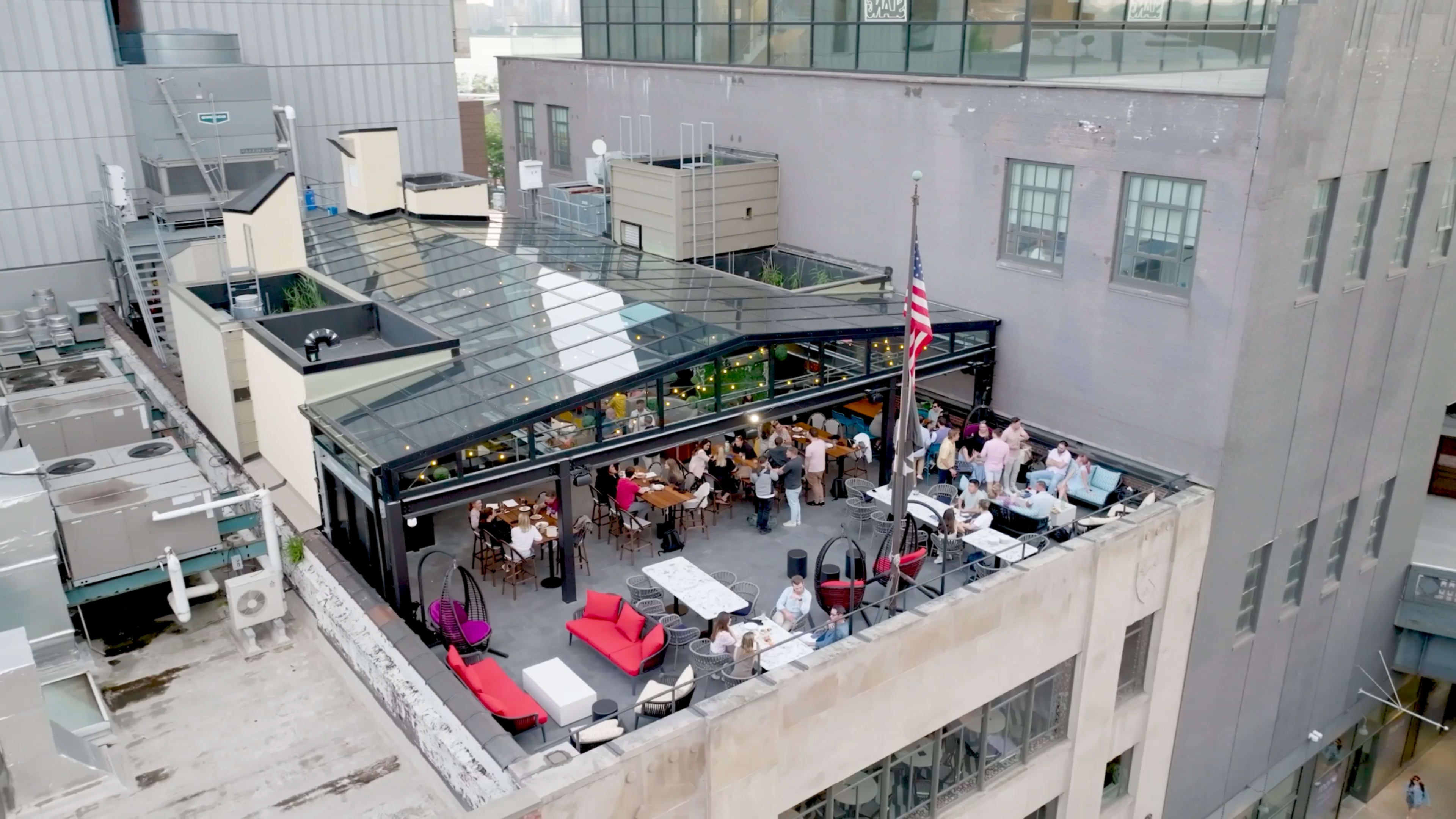 The image shows a rooftop terrace filled with diners sitting at tables under a transparent canopy, with several people enjoying the outdoor space.